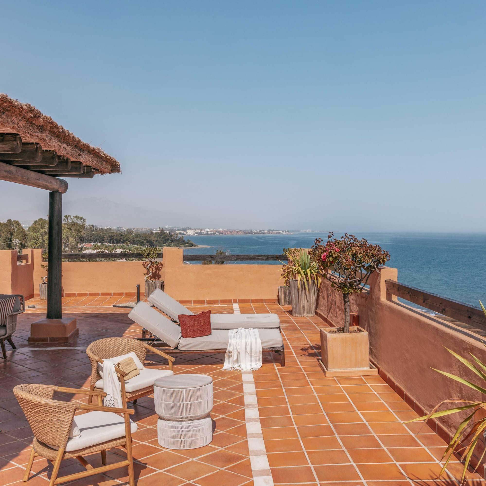Ocean view rooftop terrace with sunbeds, lounge chairs, and thatched roof.