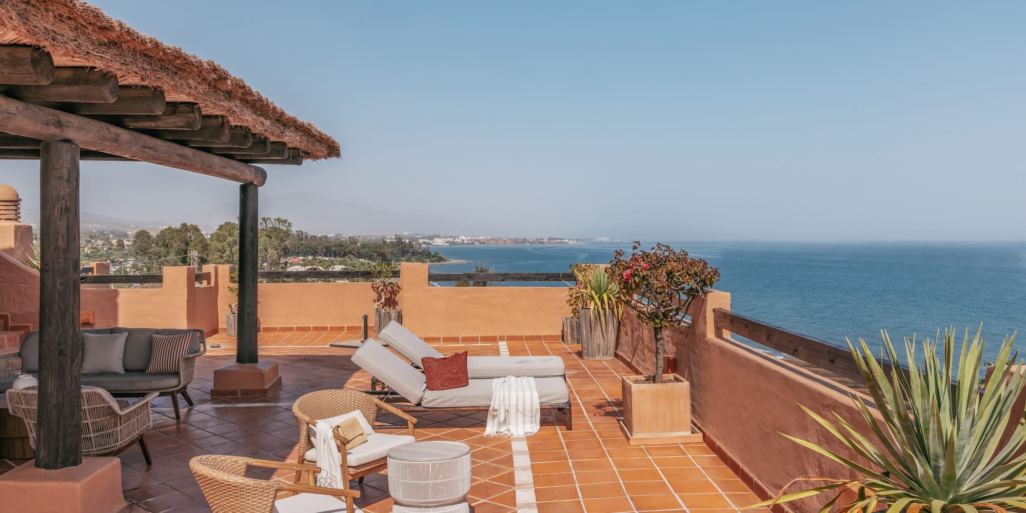 Ocean view rooftop terrace with sunbeds, lounge chairs, and thatched roof.