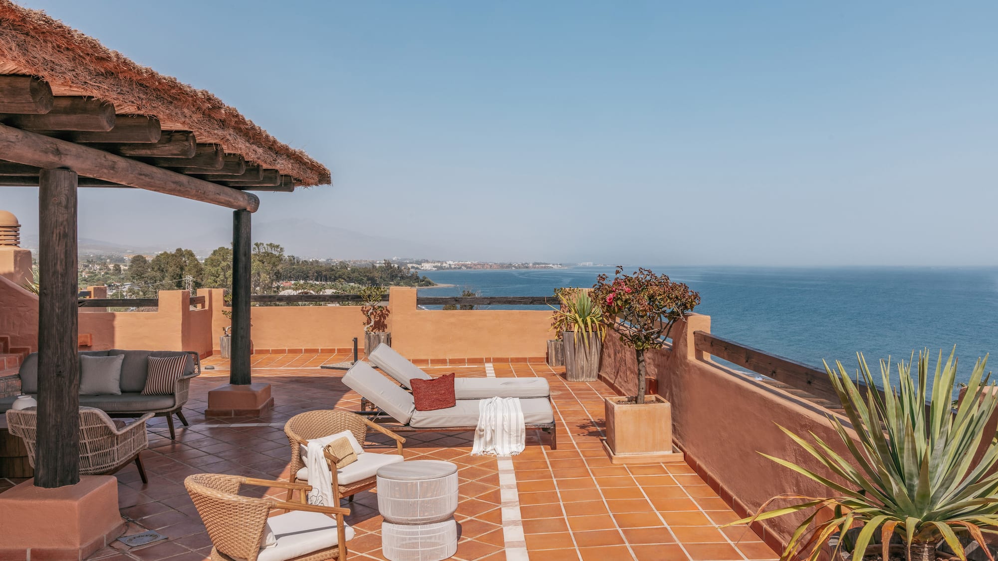 Ocean view rooftop terrace with sunbeds, lounge chairs, and thatched roof.