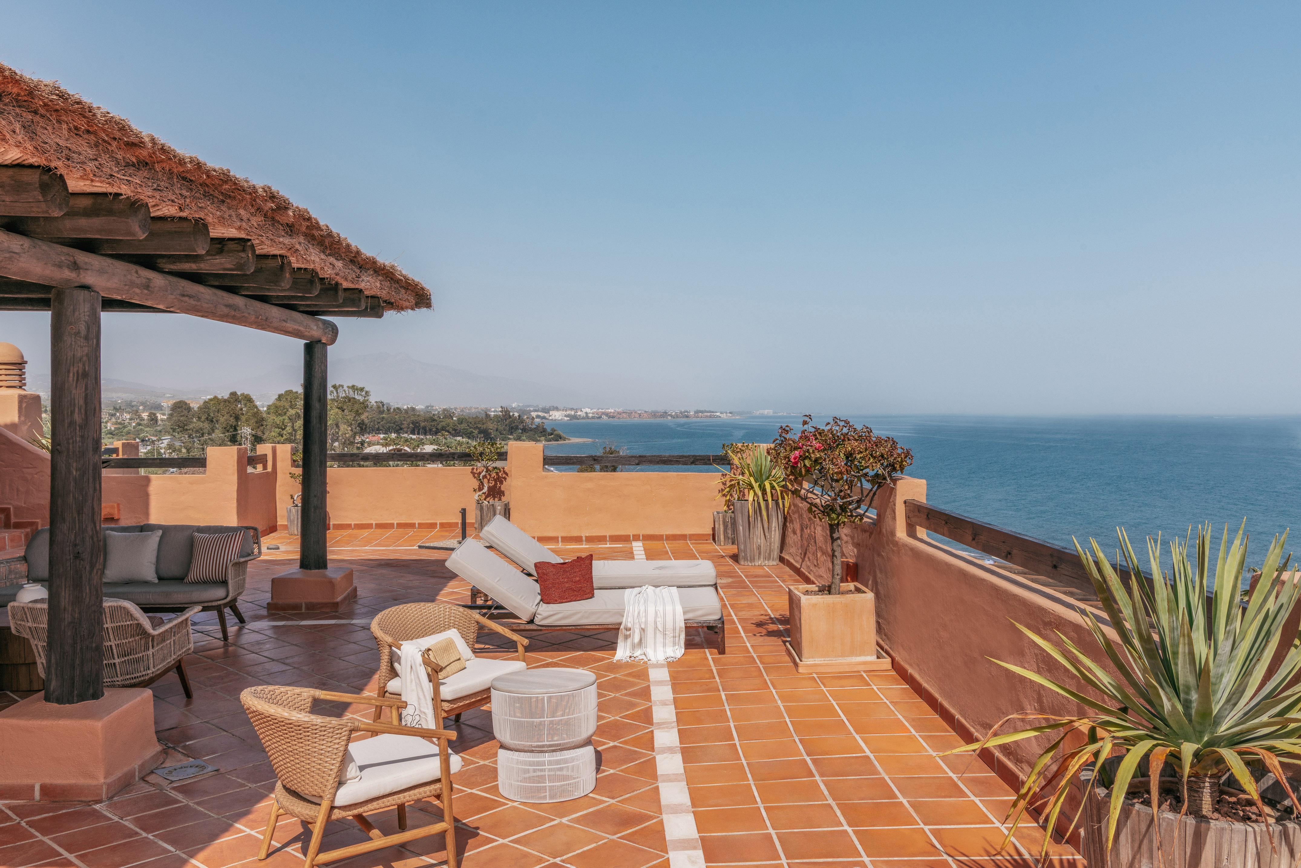 Ocean view rooftop terrace with sunbeds, lounge chairs, and thatched roof.