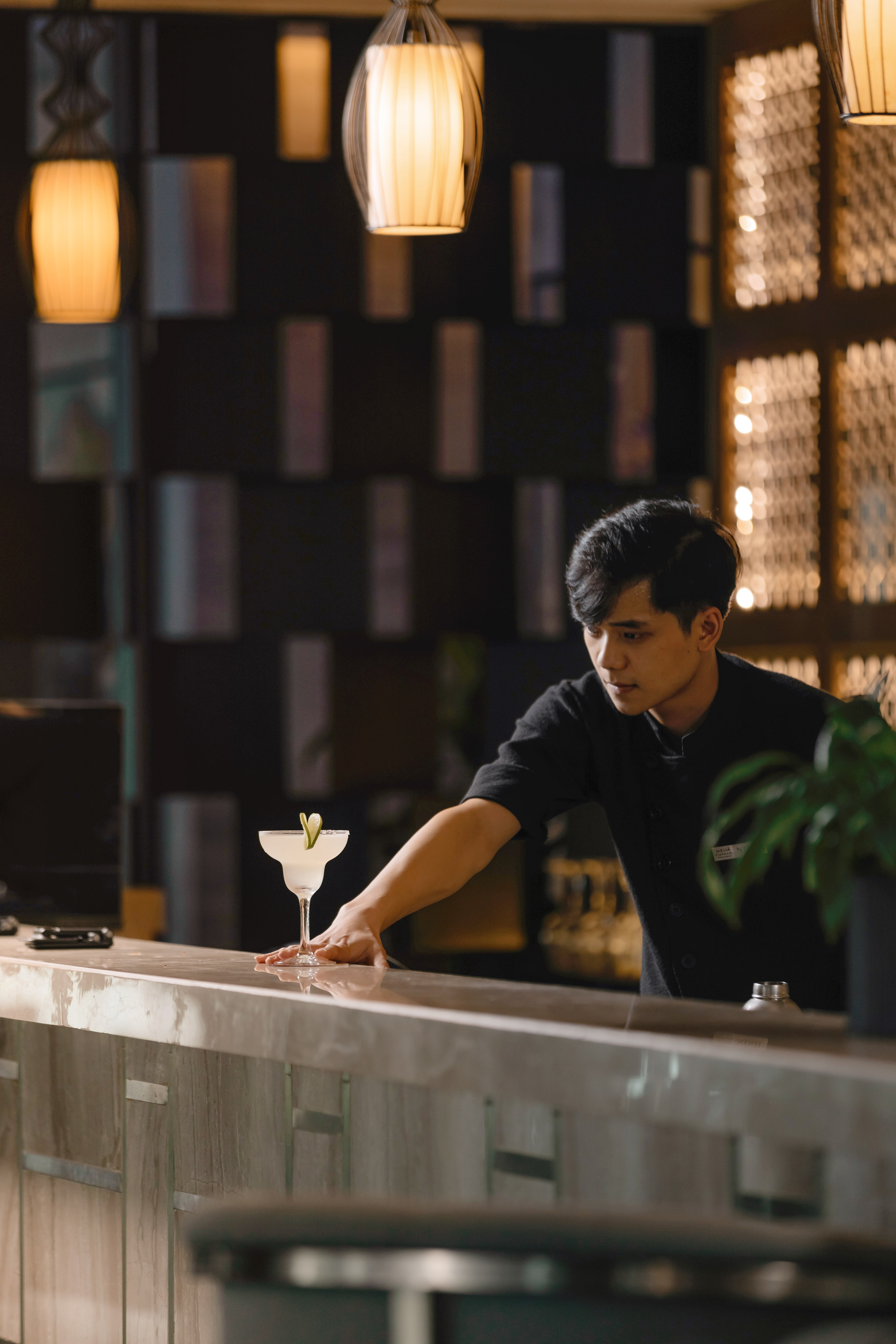 Male bartender with a margarita cocktail on a modern bar counter.