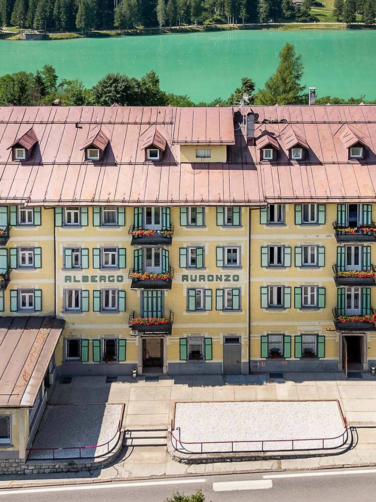 Yellow Albergo Auronzo hotel overlooking turquoise Lake Auronzo and forest.