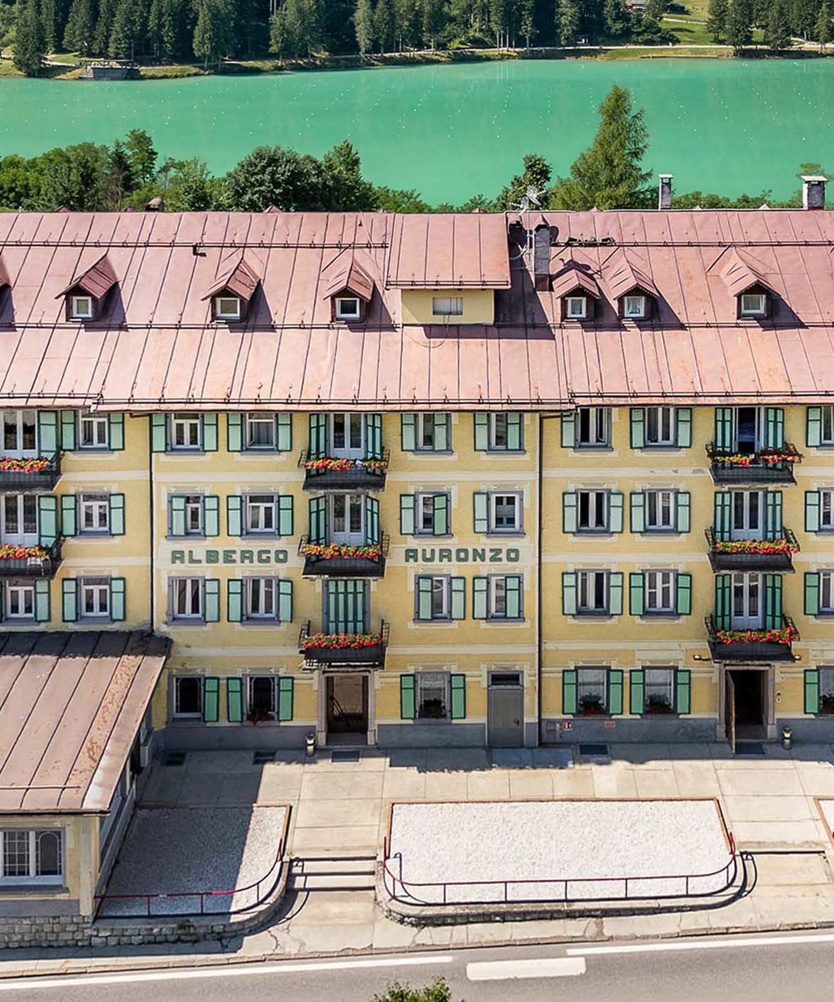 Yellow Albergo Auronzo hotel overlooking turquoise Lake Auronzo and forest.