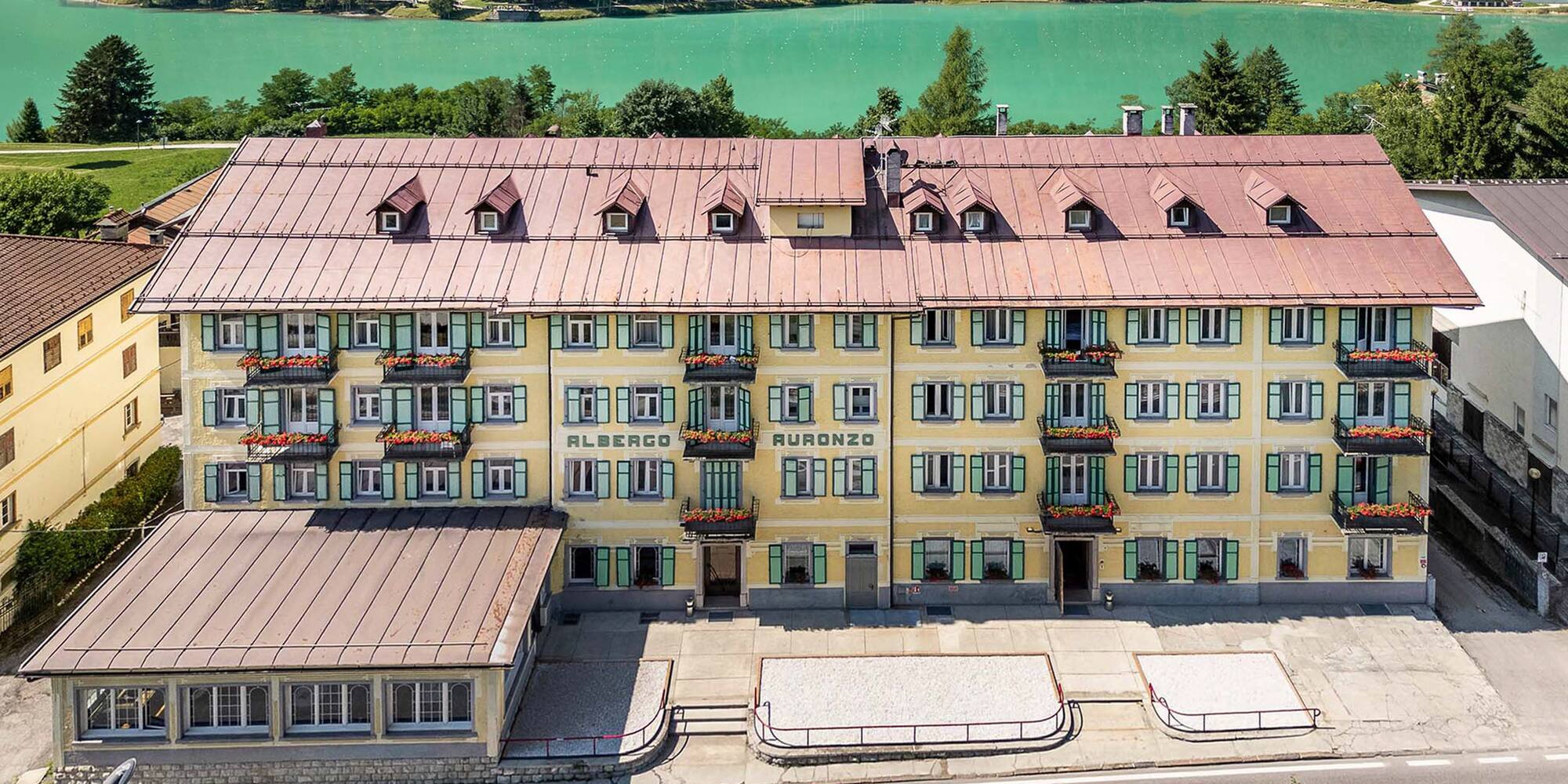 Albergo Auronzo: yellow hotel with green shutters, red roof, and turquoise lake.