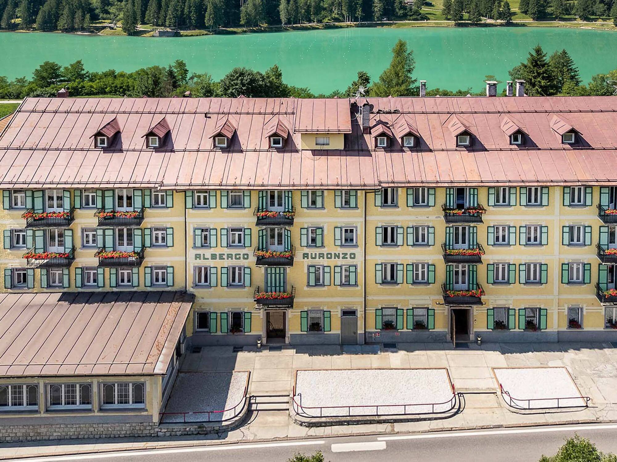 Albergo Auronzo hotel overlooking turquoise lake and pine forest.