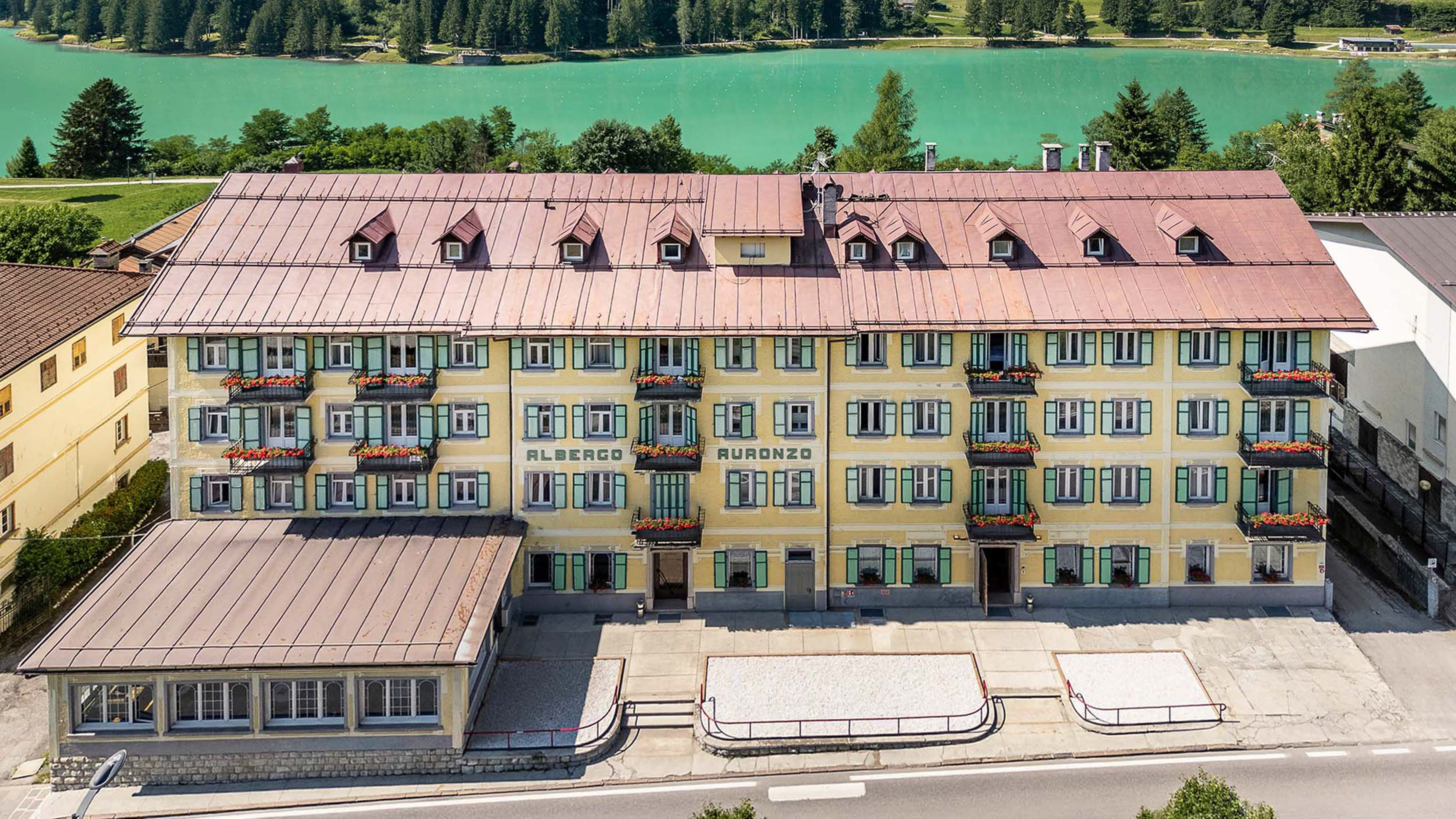 Albergo Auronzo hotel overlooking turquoise lake and pine forest.