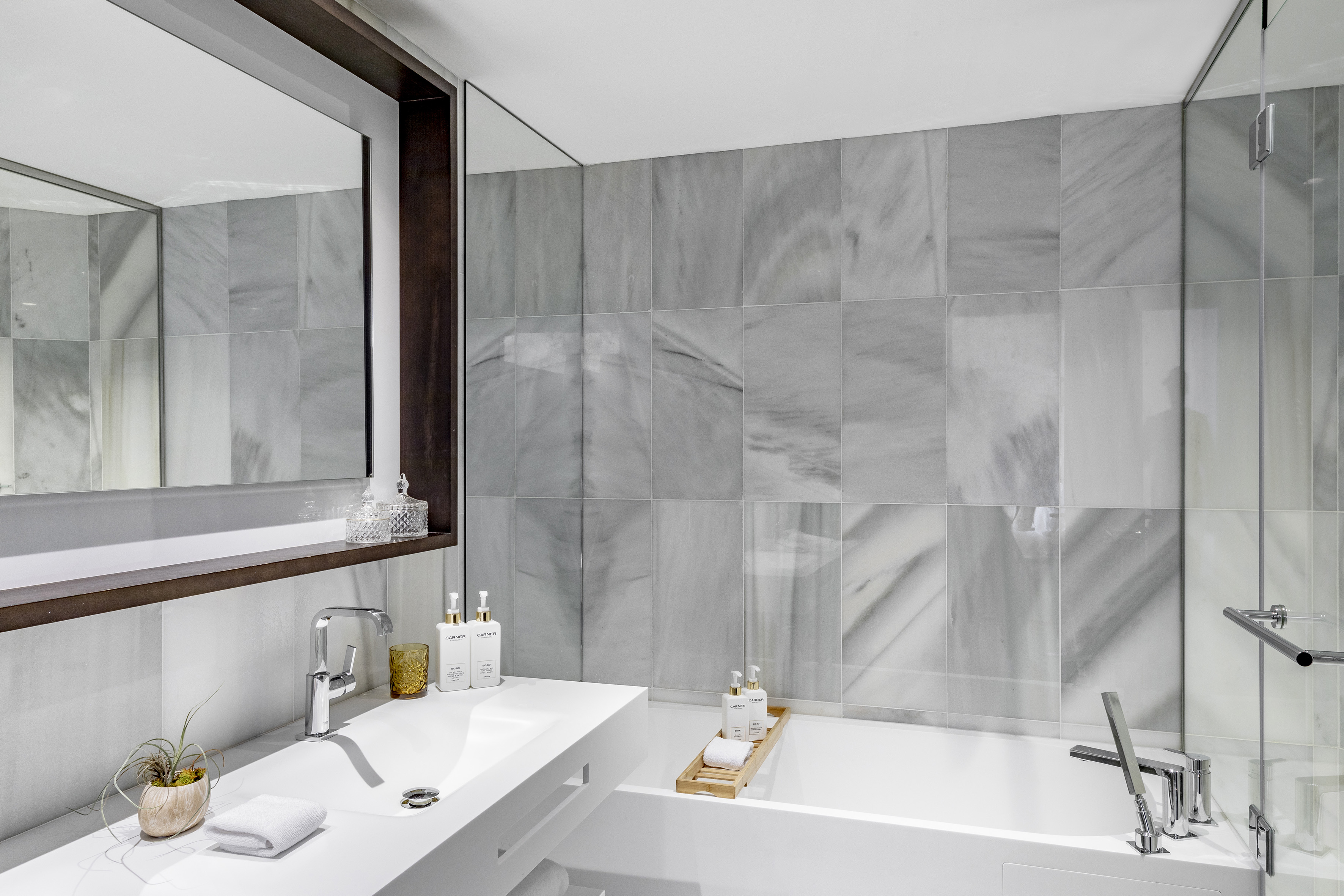 Modern bathroom with white sink, bathtub, and grey marble wall tiles.