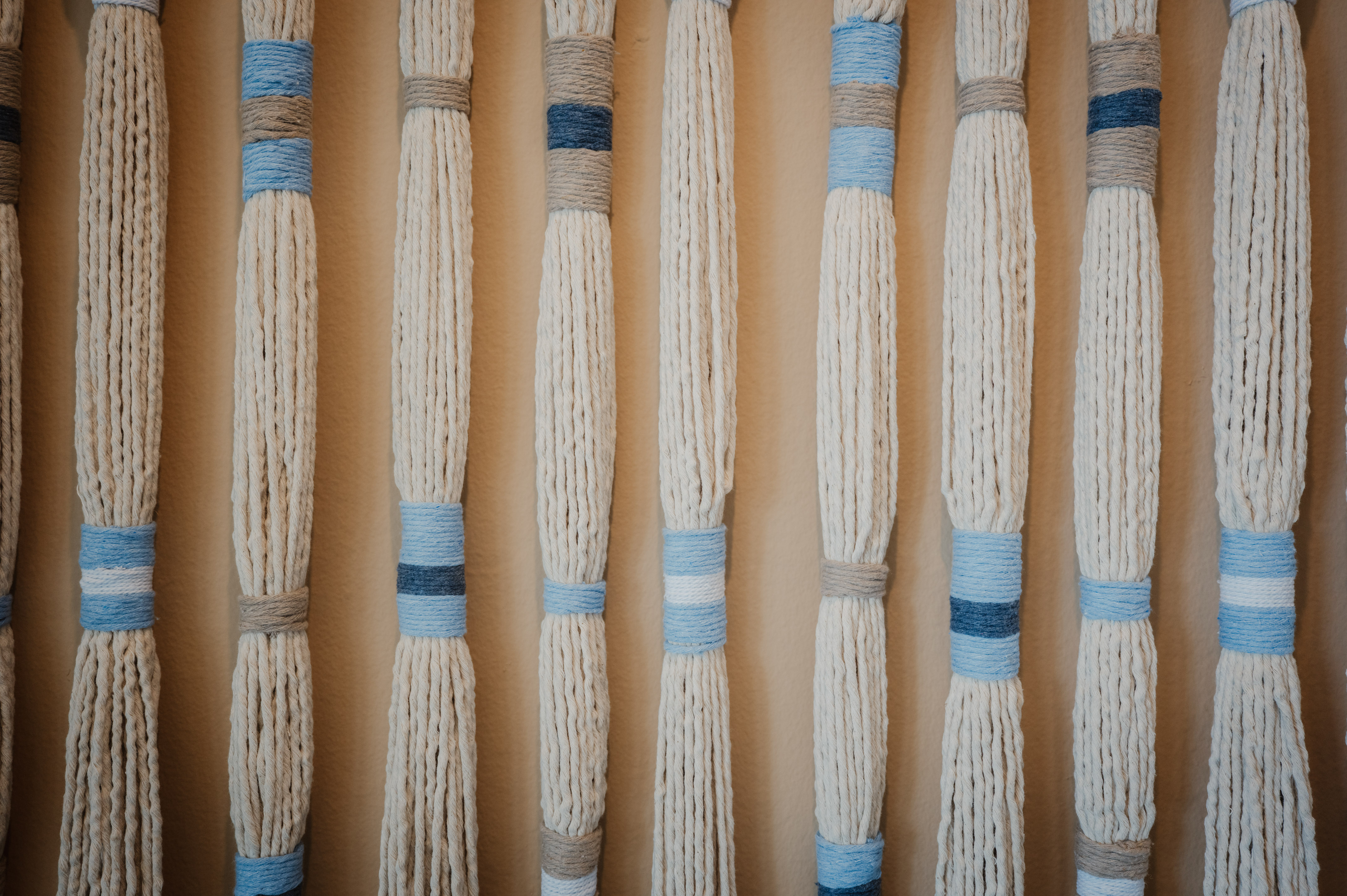 Arte de pared macramé con hilos crema, bandas azules y grises.