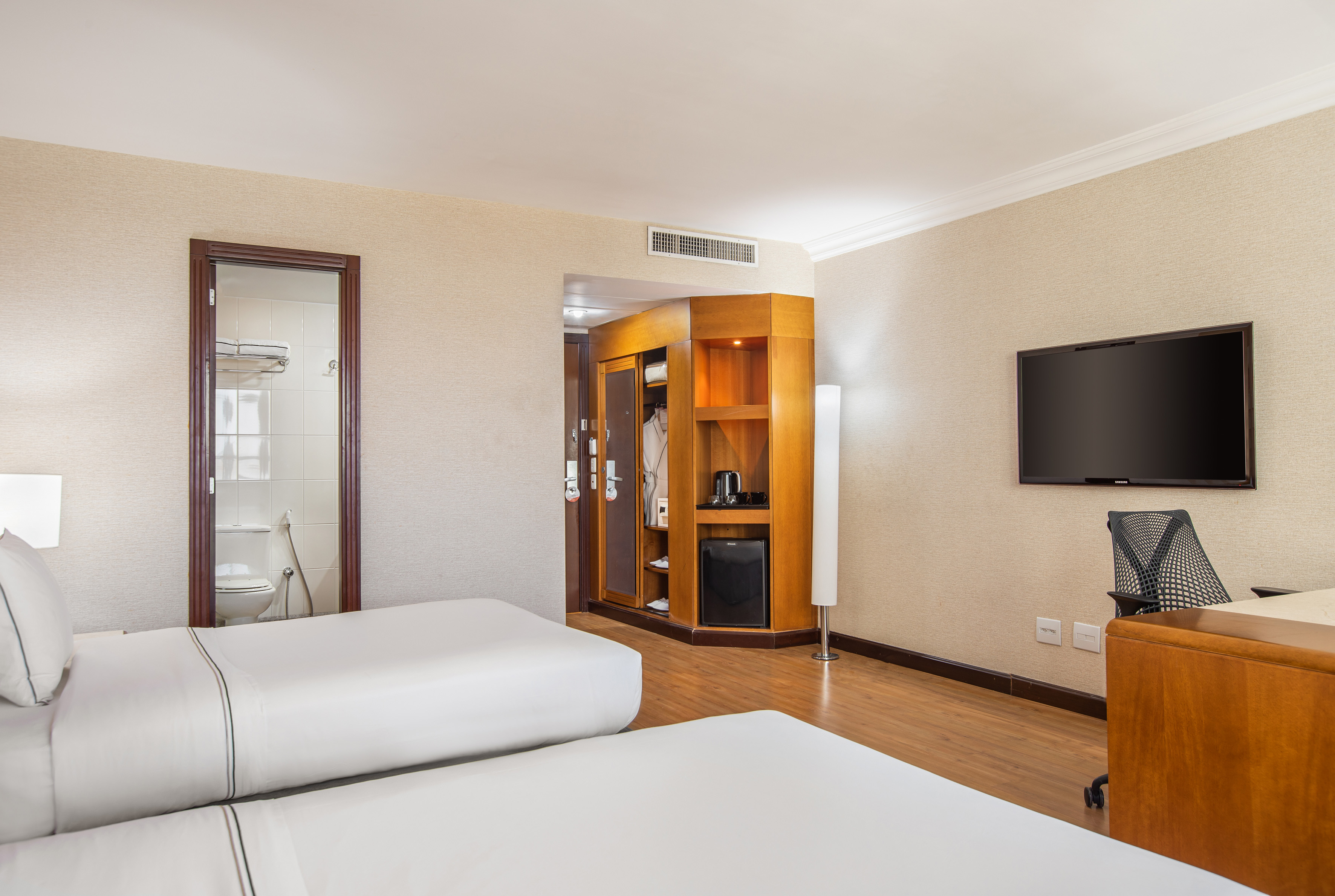 Hotel room with two twin beds, minibar, TV, and bathroom entrance.