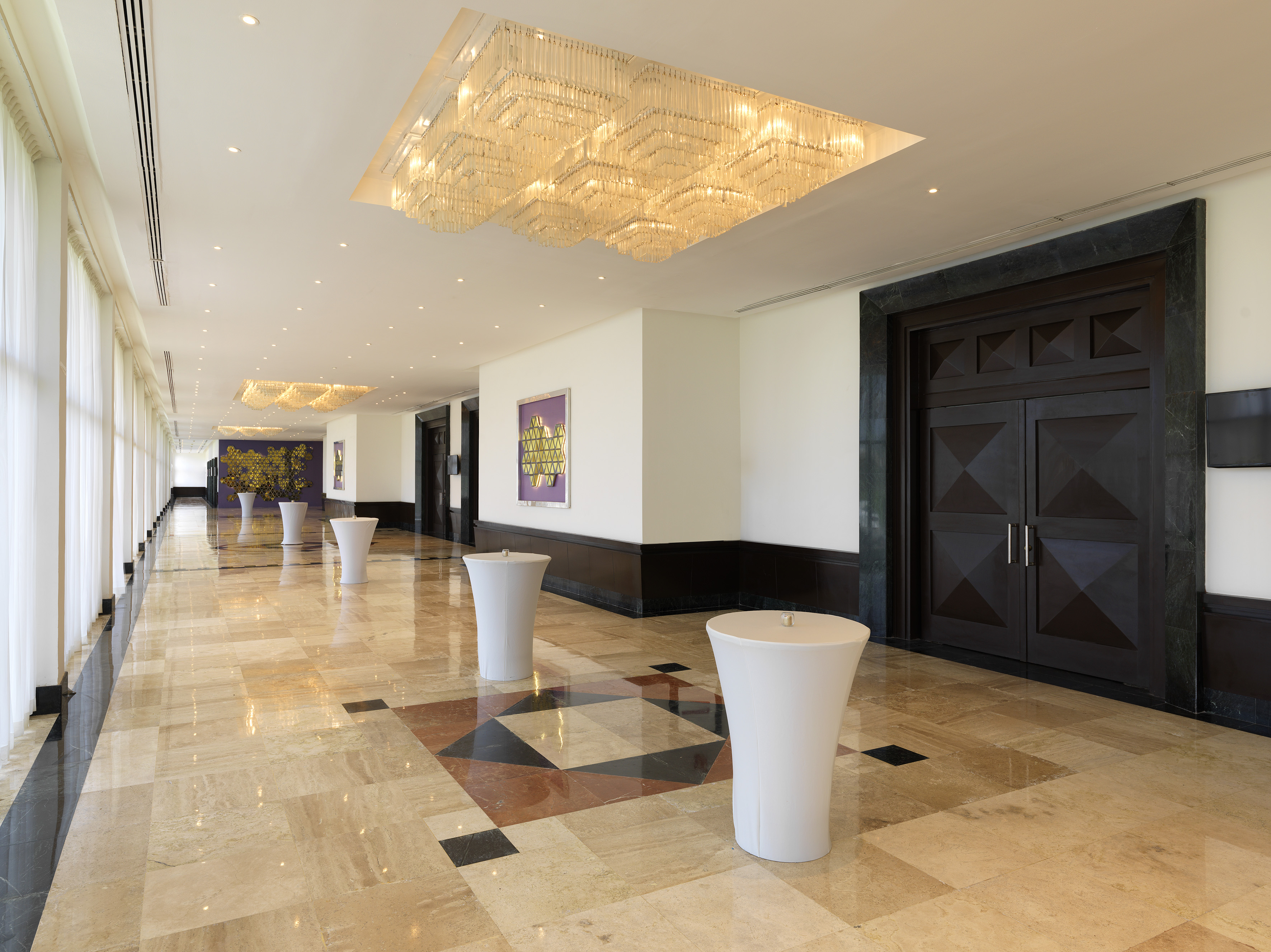 Luxury corridor with marble flooring, crystal chandeliers, and dark doors.