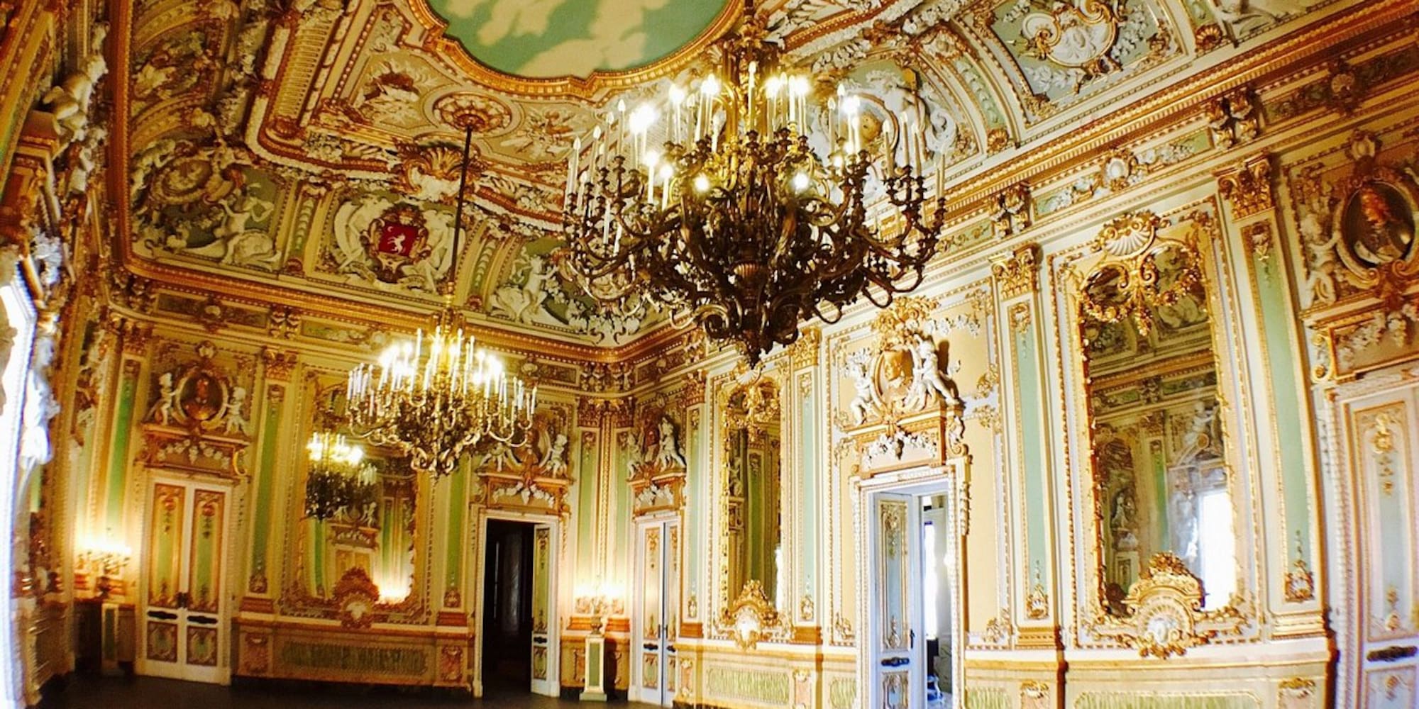 Ornate grand ballroom with golden decor, chandeliers, and fresco ceiling.
