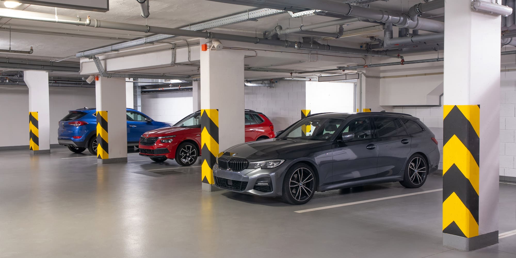 Underground parking garage, parked cars, concrete pillars with chevron markings.