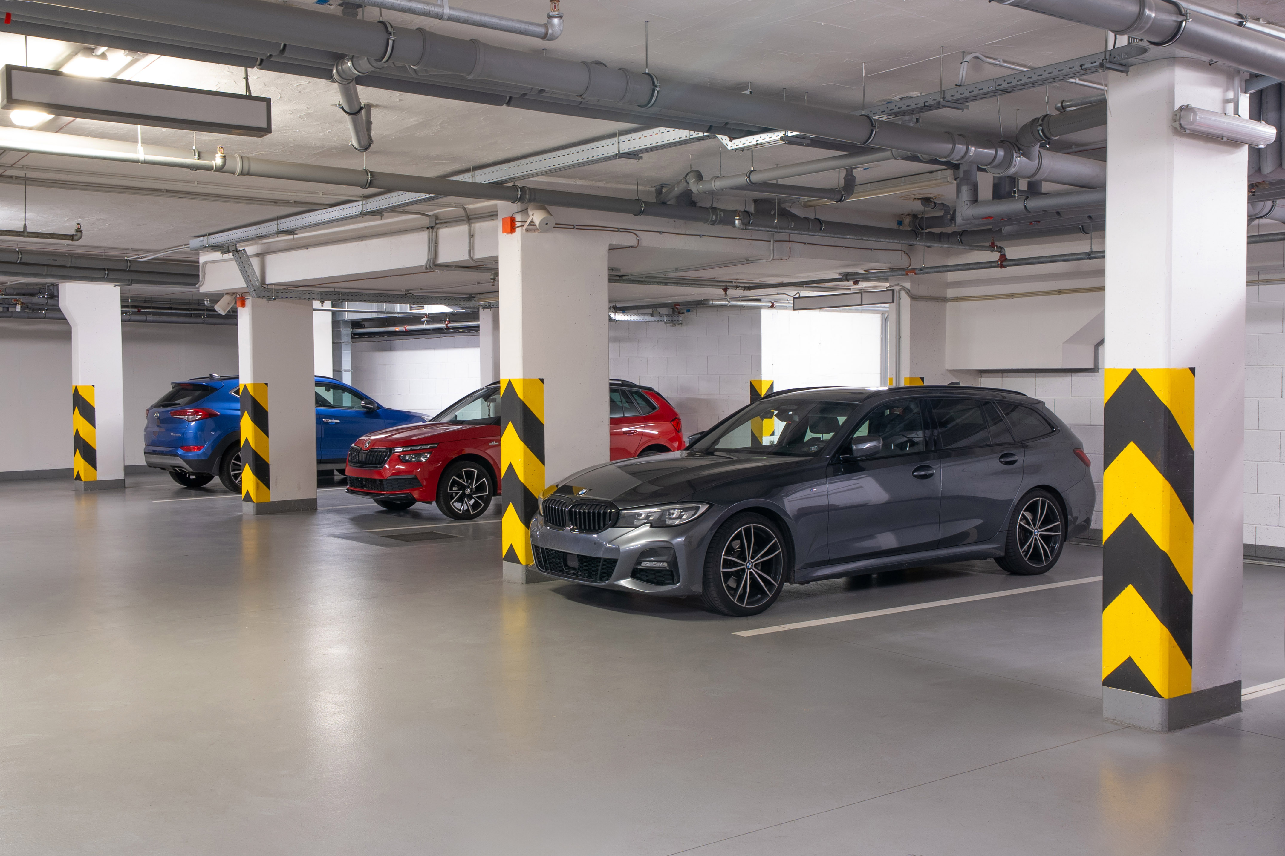 Underground parking garage, parked cars, concrete pillars with chevron markings.