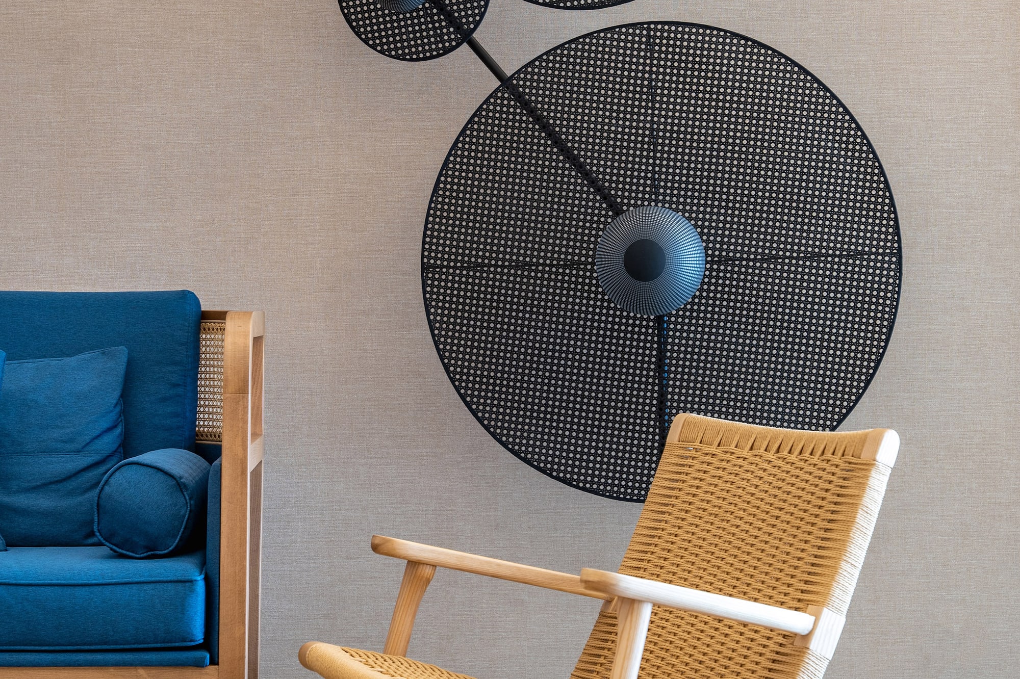 Modern living room with blue sofa, rattan armchair, cane wall art, and woven rug.
