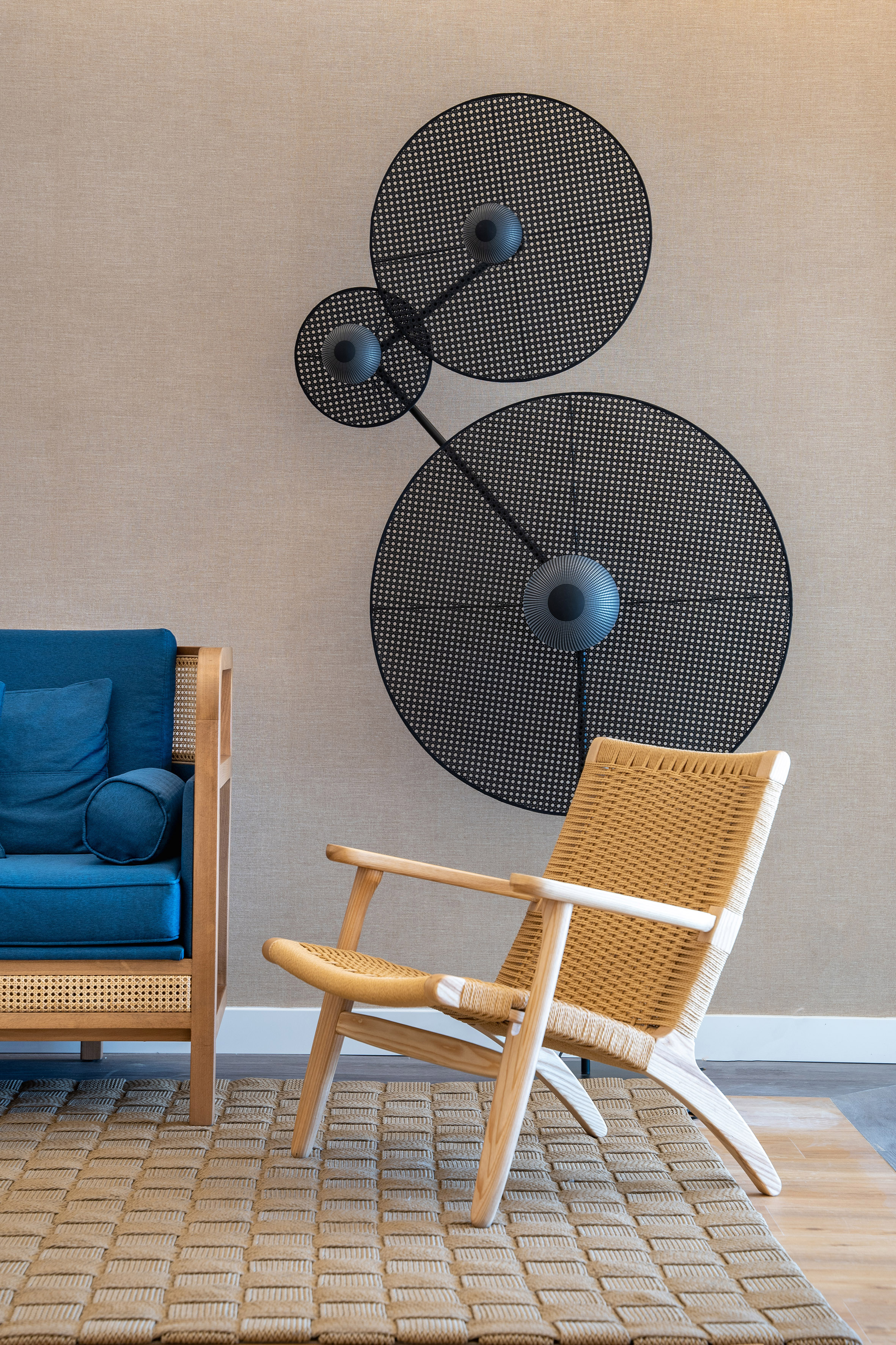 Modern living room with blue sofa, rattan armchair, cane wall art, and woven rug.