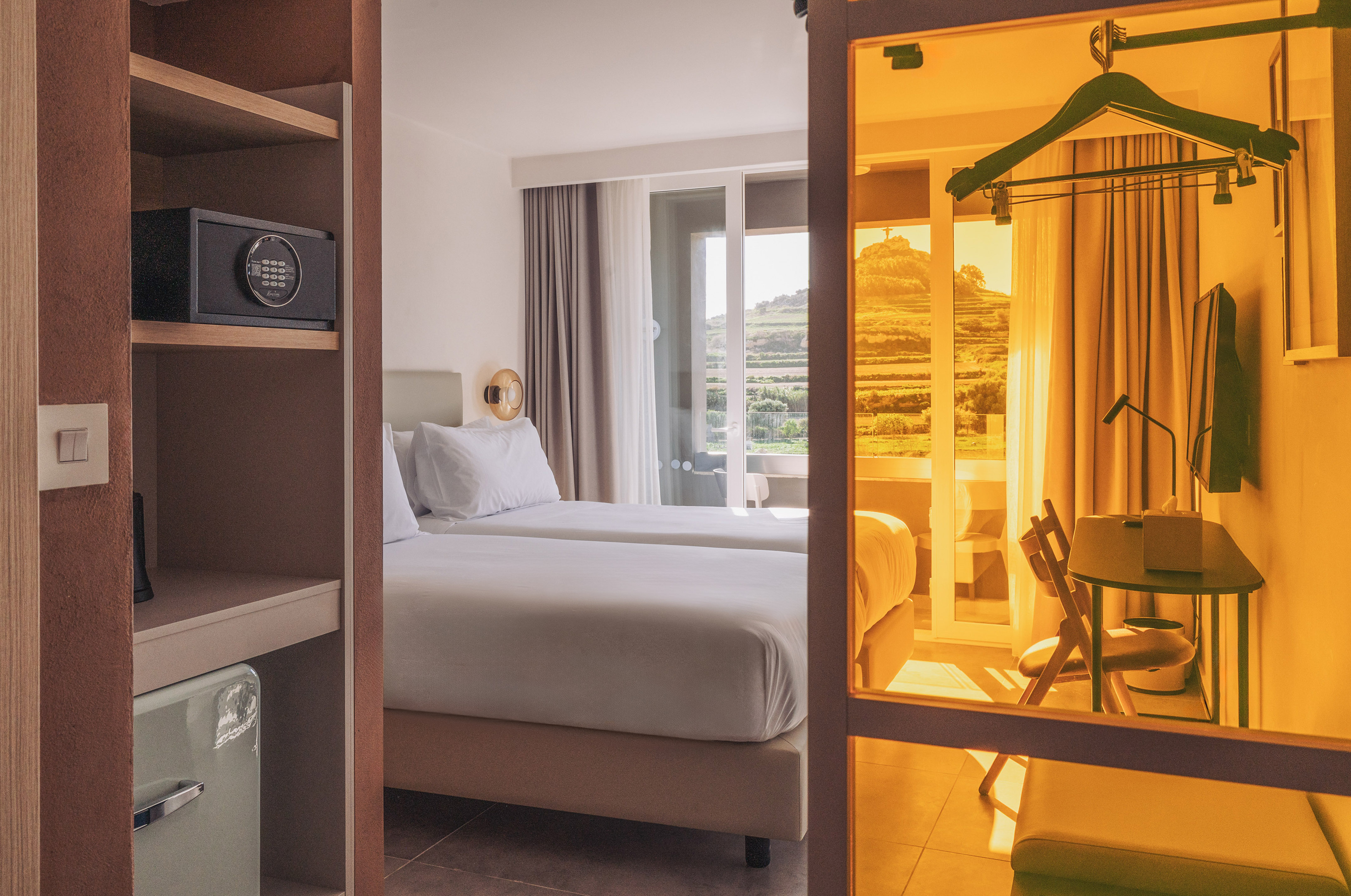 Hotel room with twin beds, balcony hill view, in-room safe, and mini-fridge.