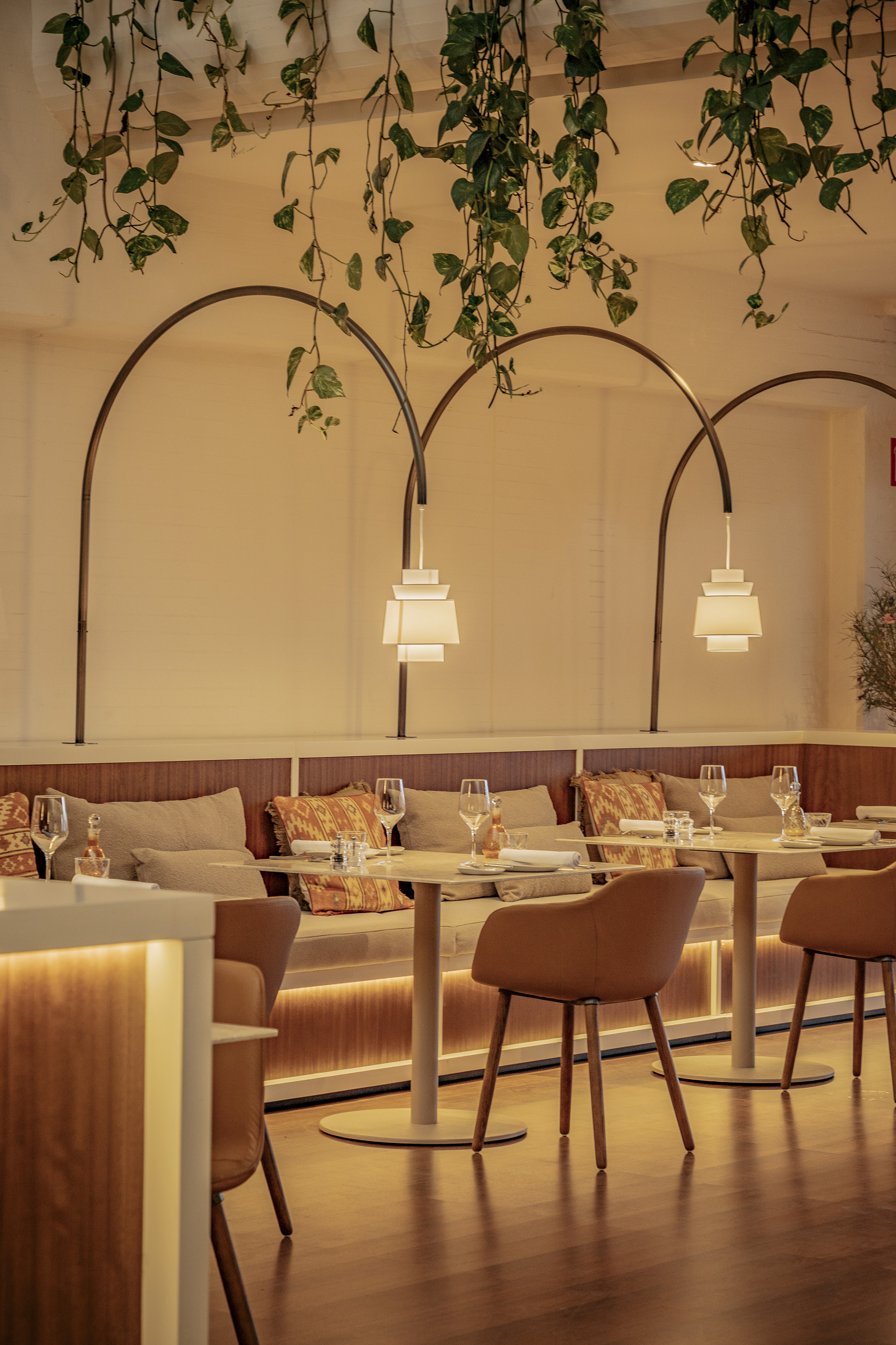 Restaurant interior: banquette seating, hanging plants, warm arched lighting.