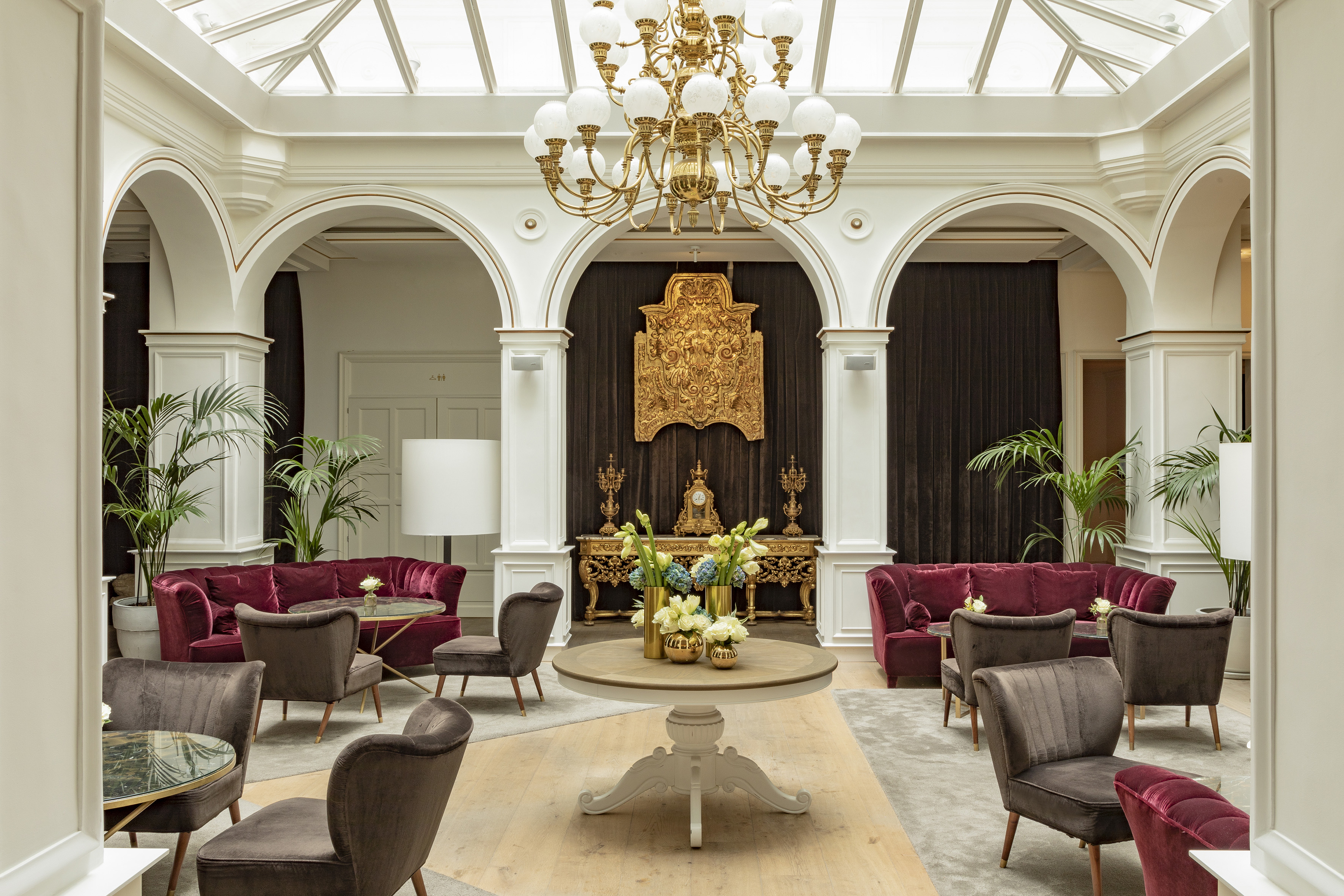 Elegant hotel lounge with chandelier, red velvet sofas, and ornate gold decor.