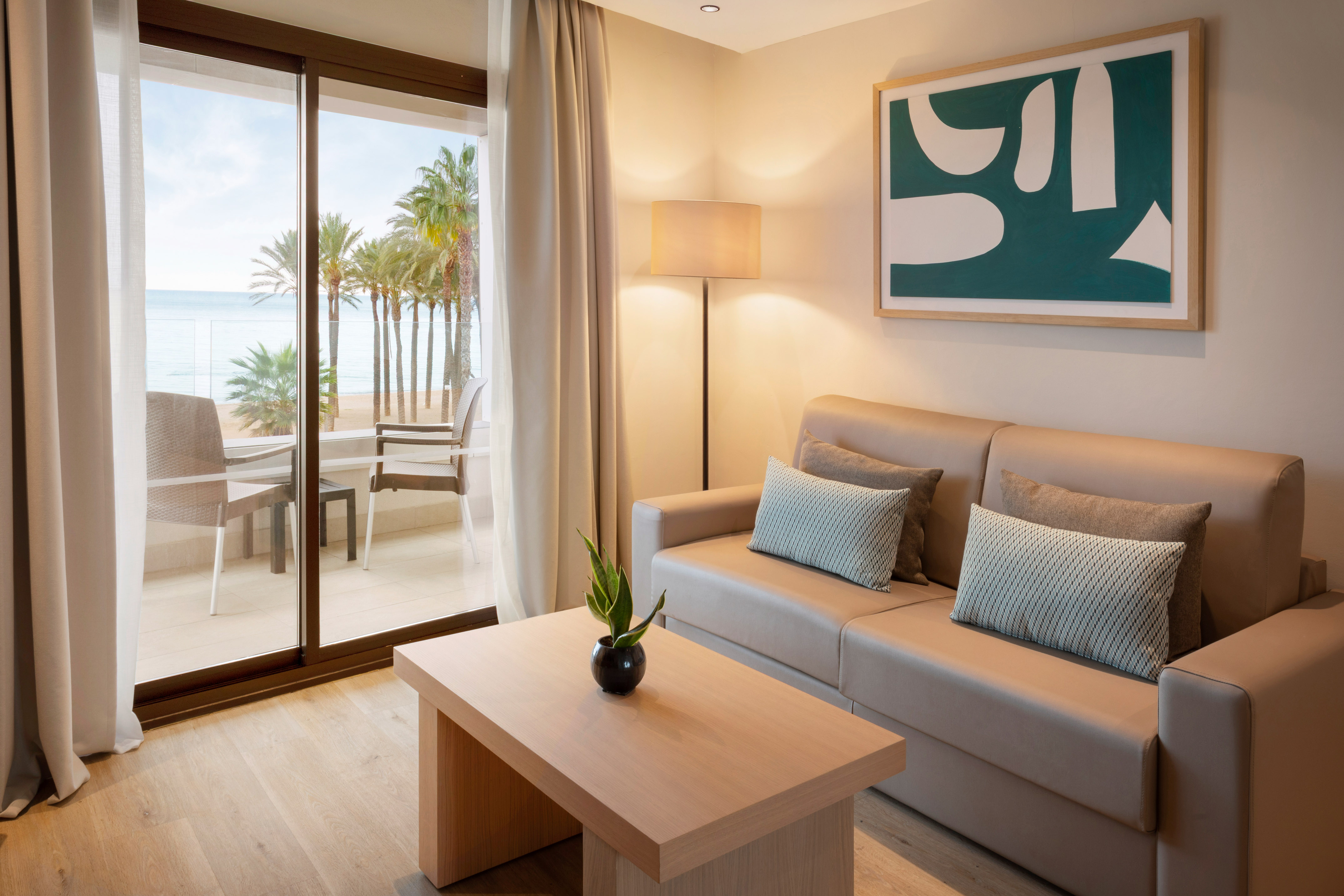 Beachfront hotel suite living room with sofa, balcony, ocean, and palm trees.