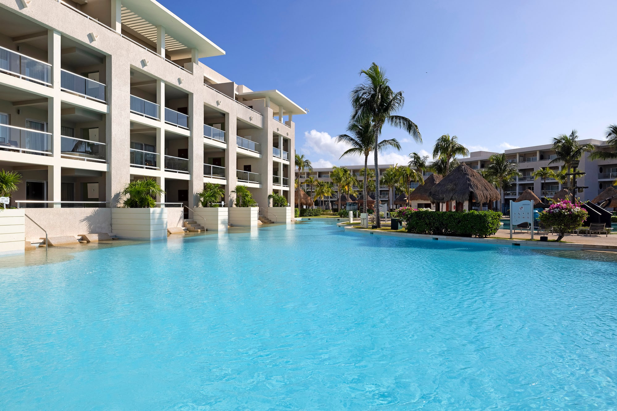 Tropical resort with spacious blue pool, hotel building, and palm trees.