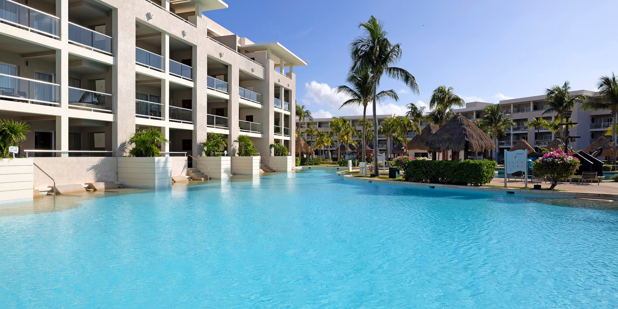Tropical resort with spacious blue pool, hotel building, and palm trees.