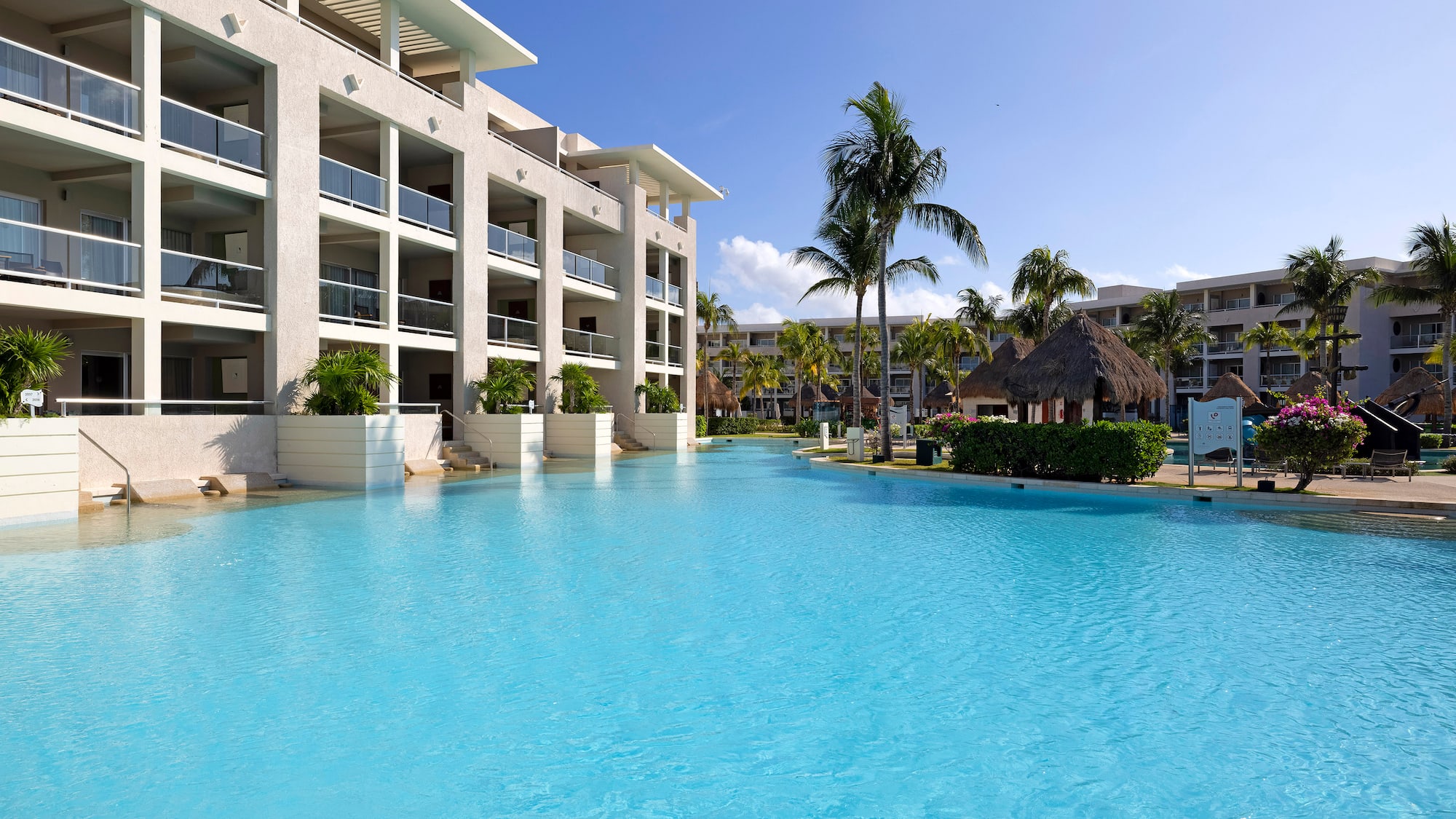 Tropical resort with spacious blue pool, hotel building, and palm trees.