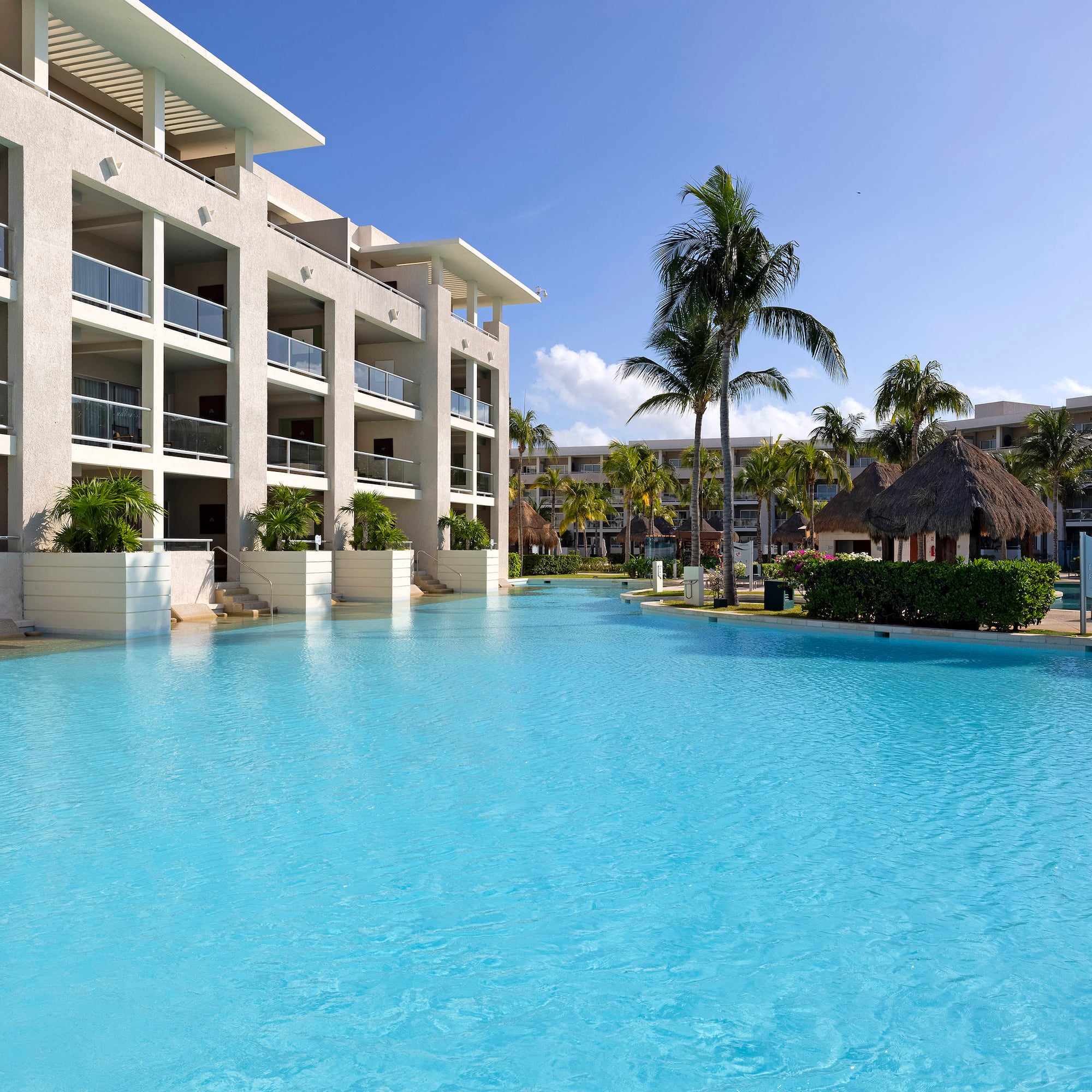 Tropical resort with spacious blue pool, hotel building, and palm trees.