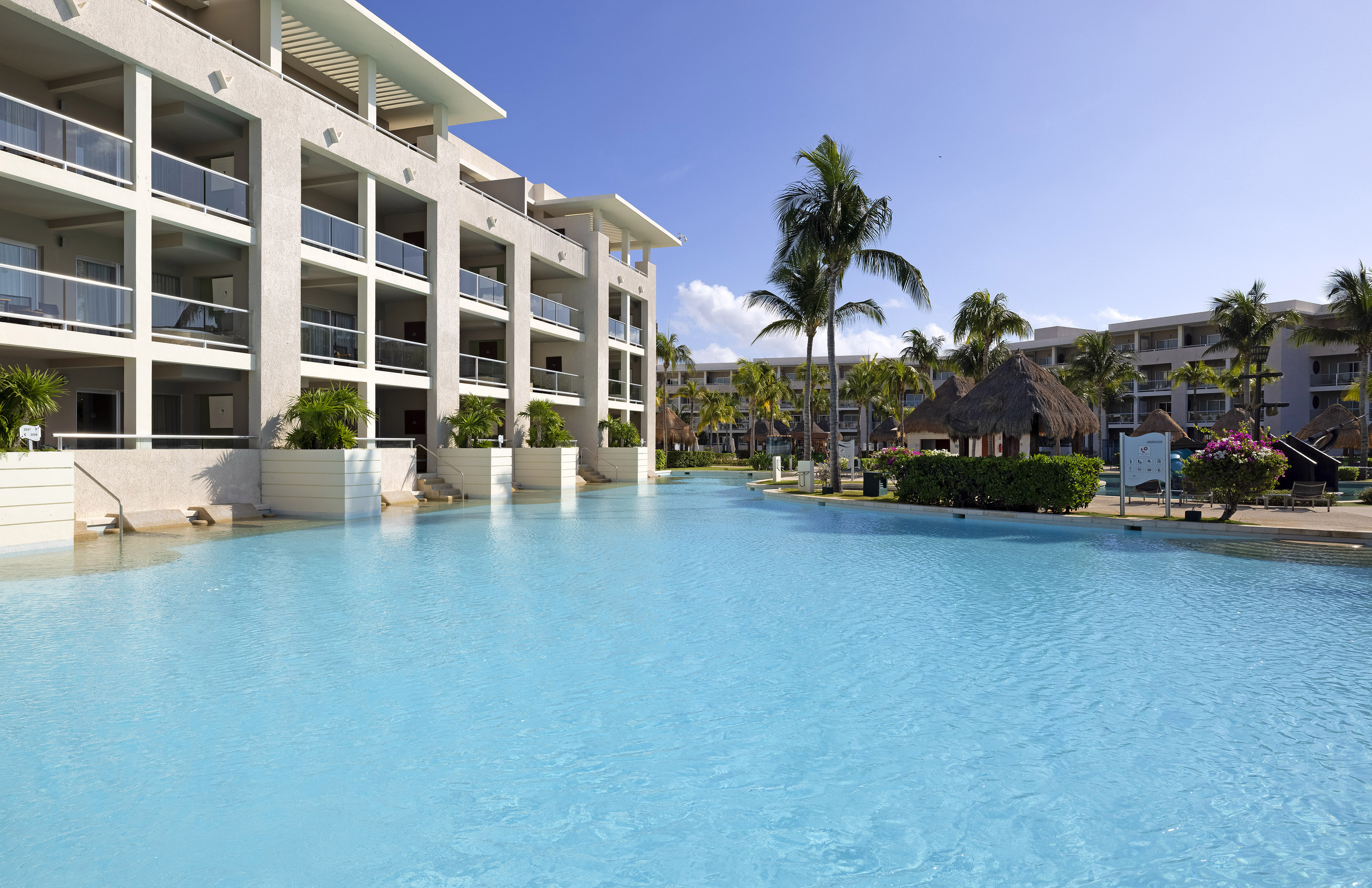 Tropical resort with spacious blue pool, hotel building, and palm trees.