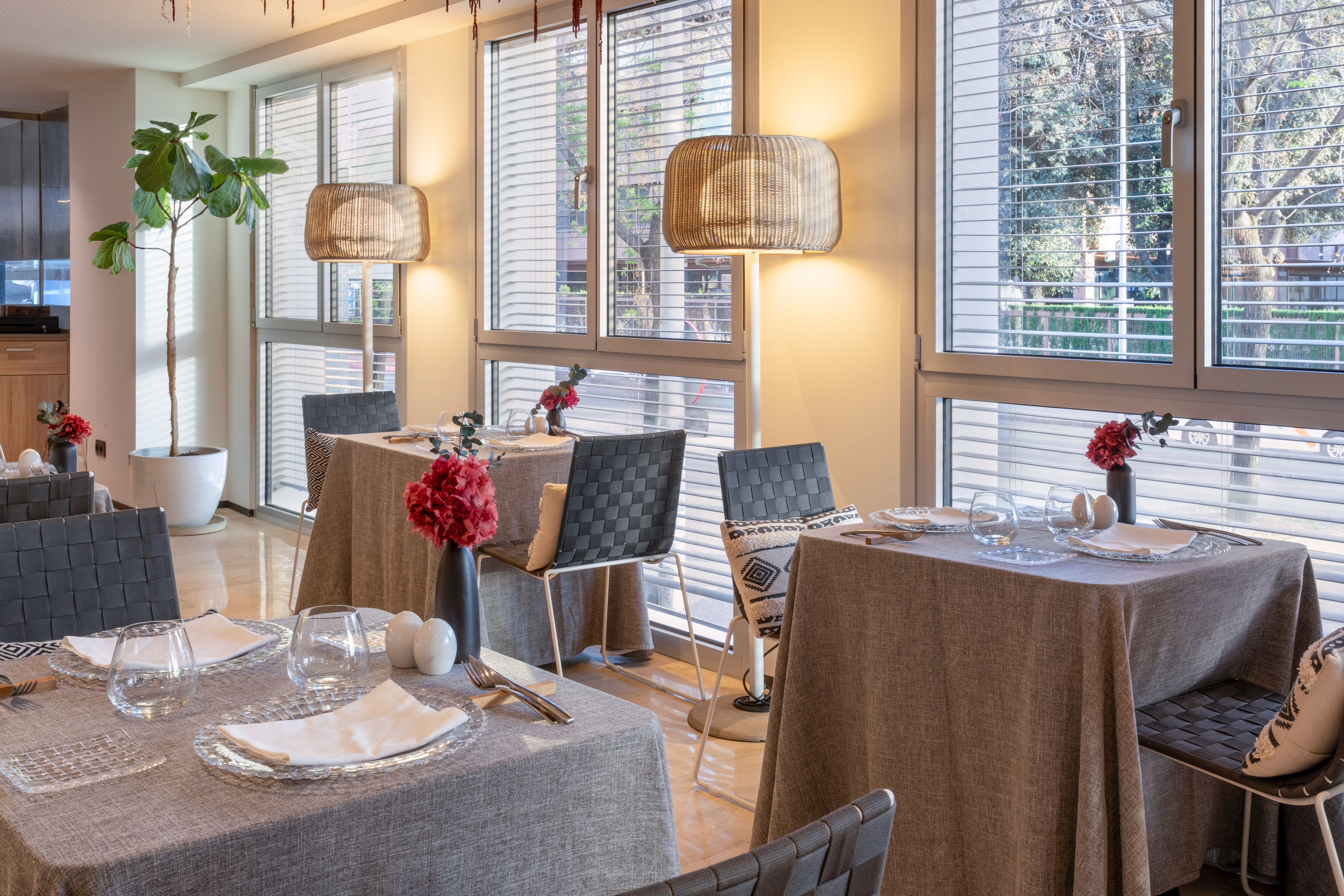 Modern restaurant dining room with set tables, large windows, woven lamps.