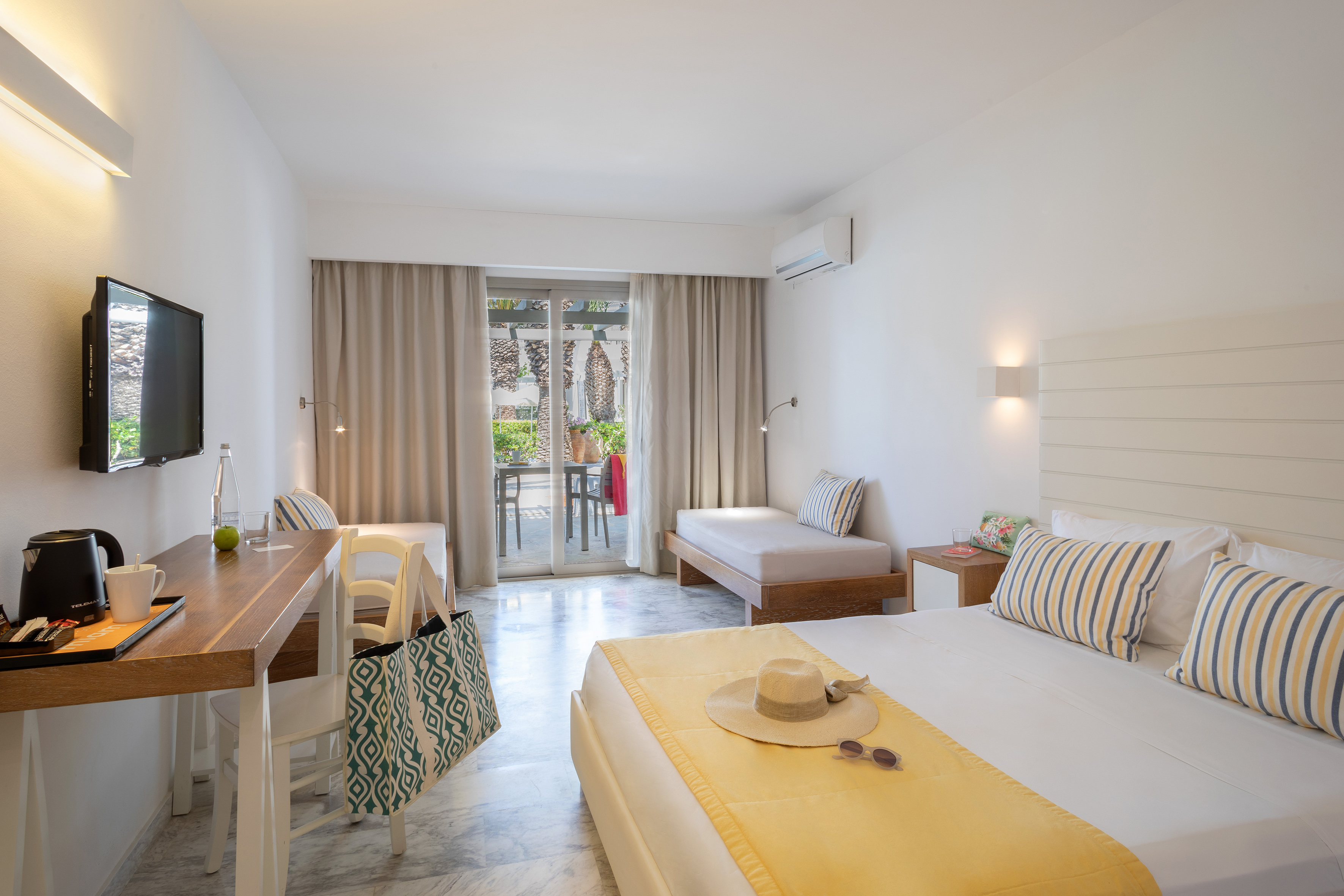 Modern hotel bedroom with bed, desk, daybed, and bright balcony view.
