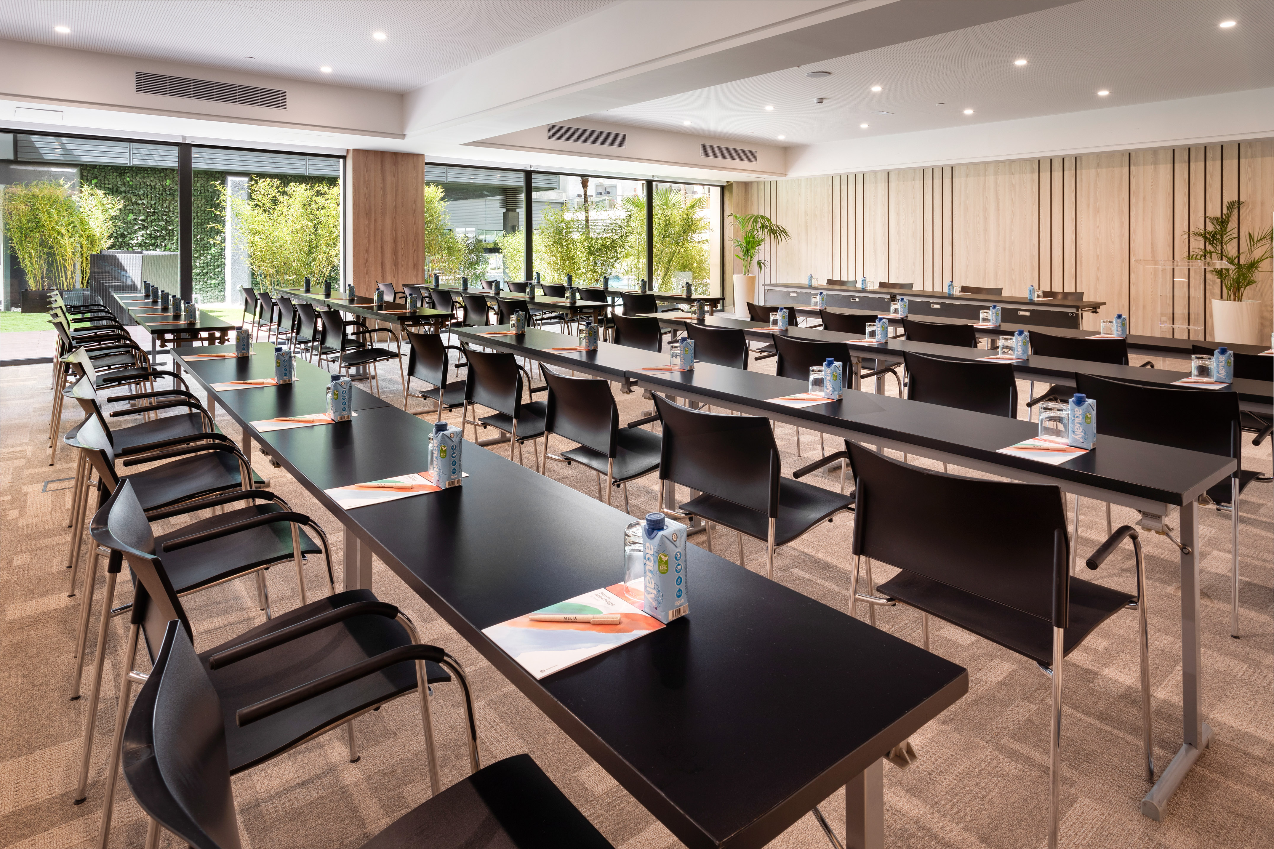 Empty conference room with classroom setup, tables, chairs, and green garden view.