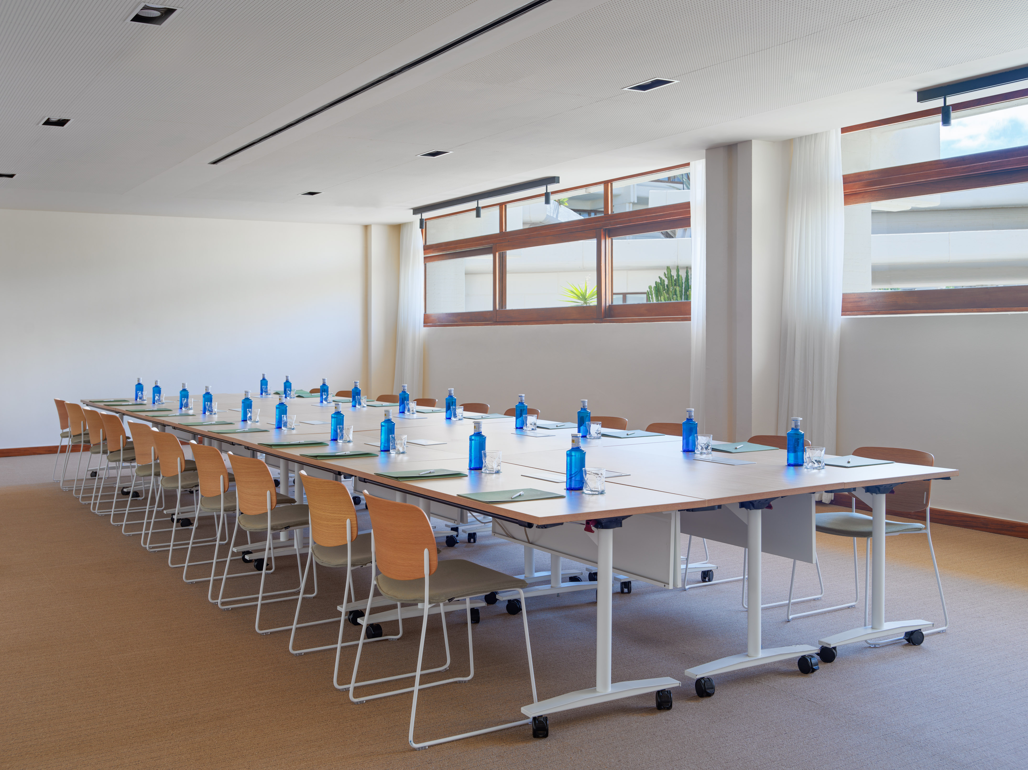 Empty modern conference room setup with U-shaped tables, chairs, and water bottles.