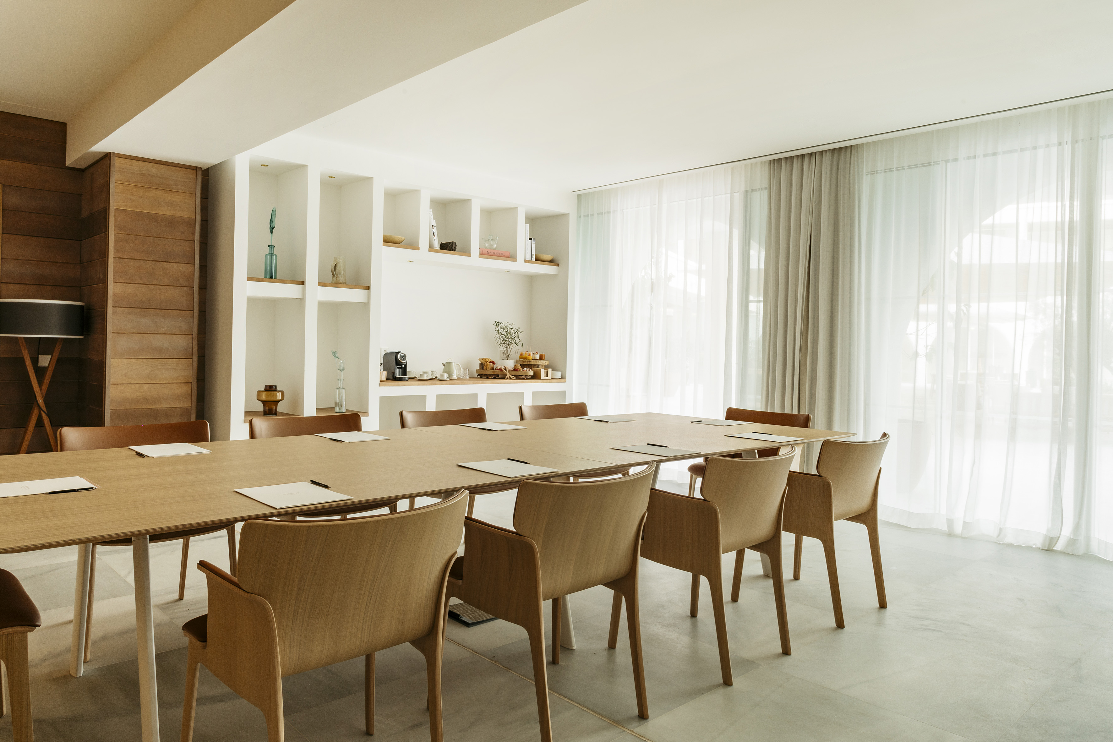 Modern bright conference room with long wood table, chairs, and window light.