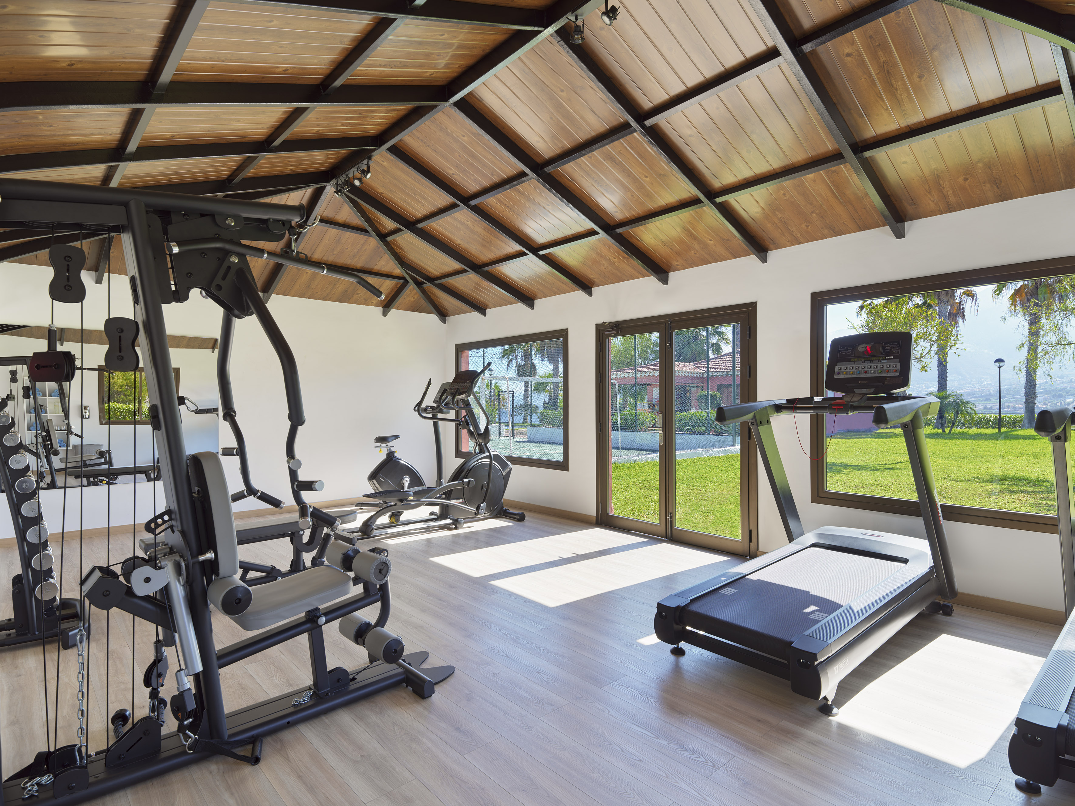 Indoor gym with treadmill, elliptical, weight machine, and outdoor garden view.
