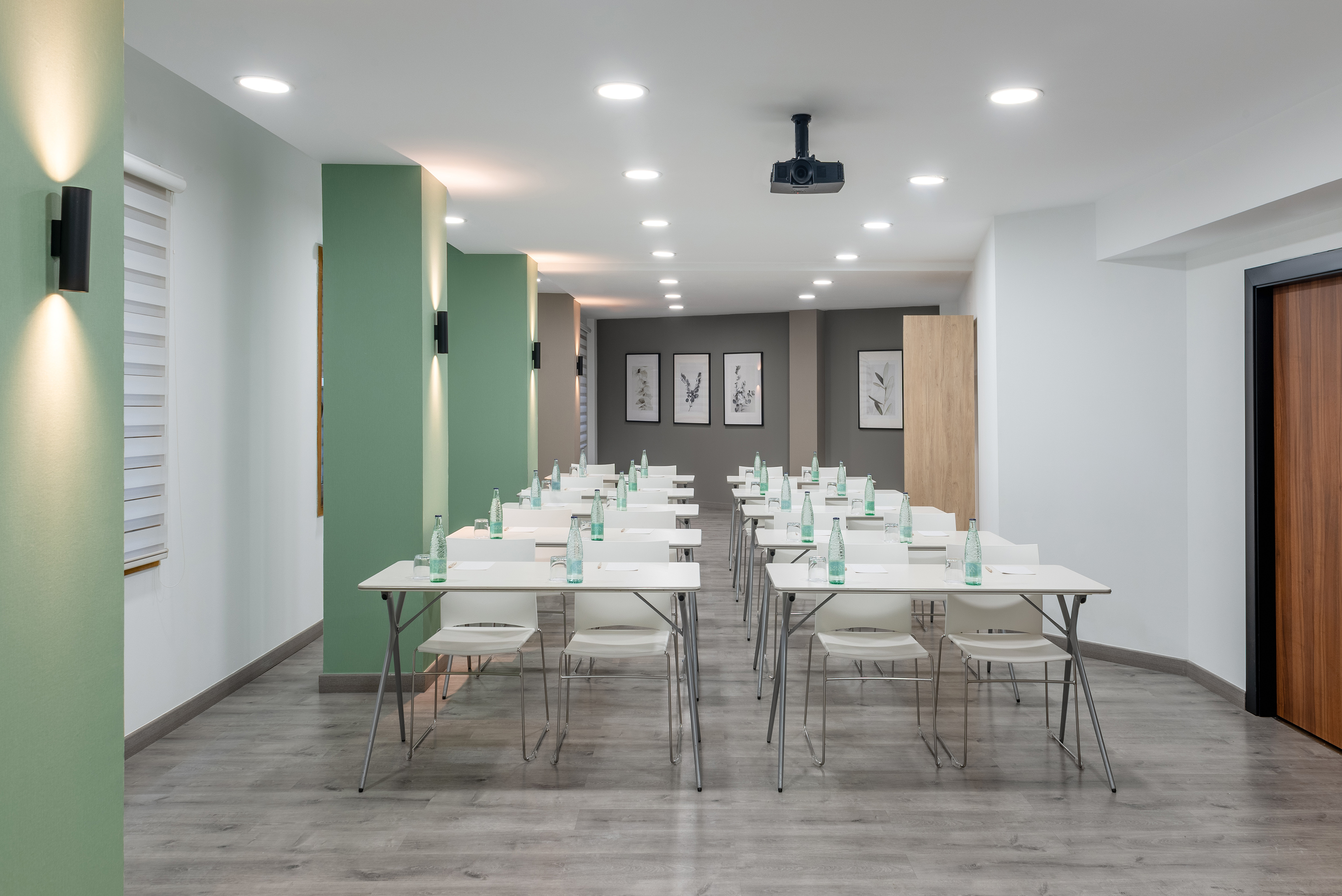 Modern meeting room with tables, chairs, water bottles, and ceiling projector.