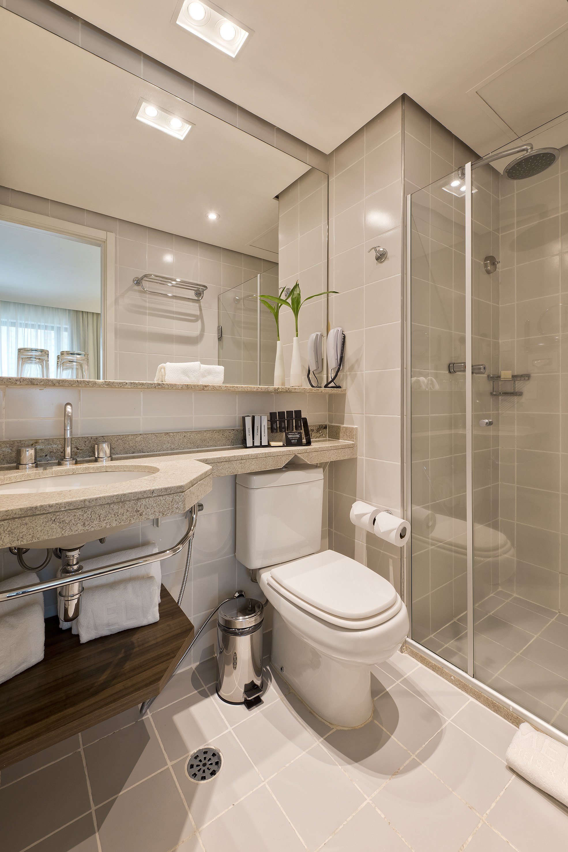 Hotel bathroom with tiled walls, granite sink, toilet, and glass shower.