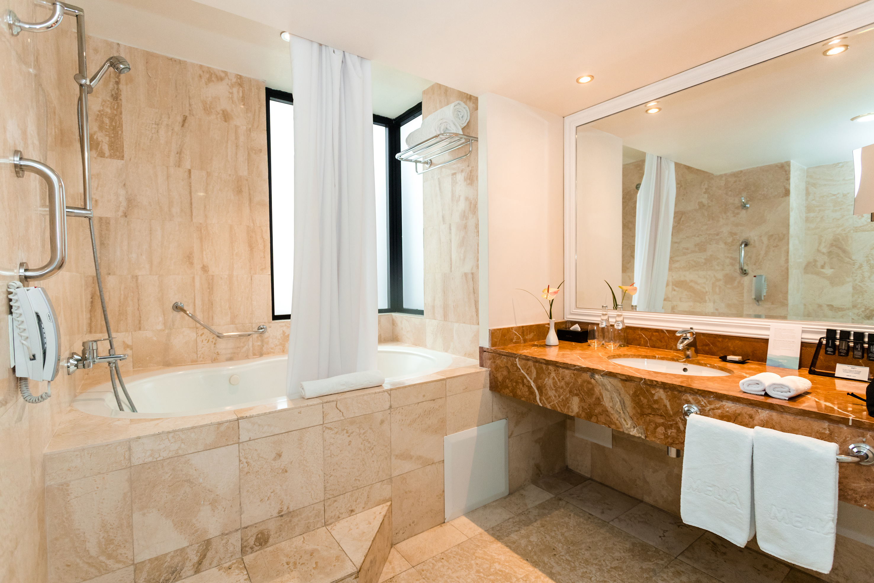 Marble hotel bathroom with spacious bathtub, shower, and vanity.