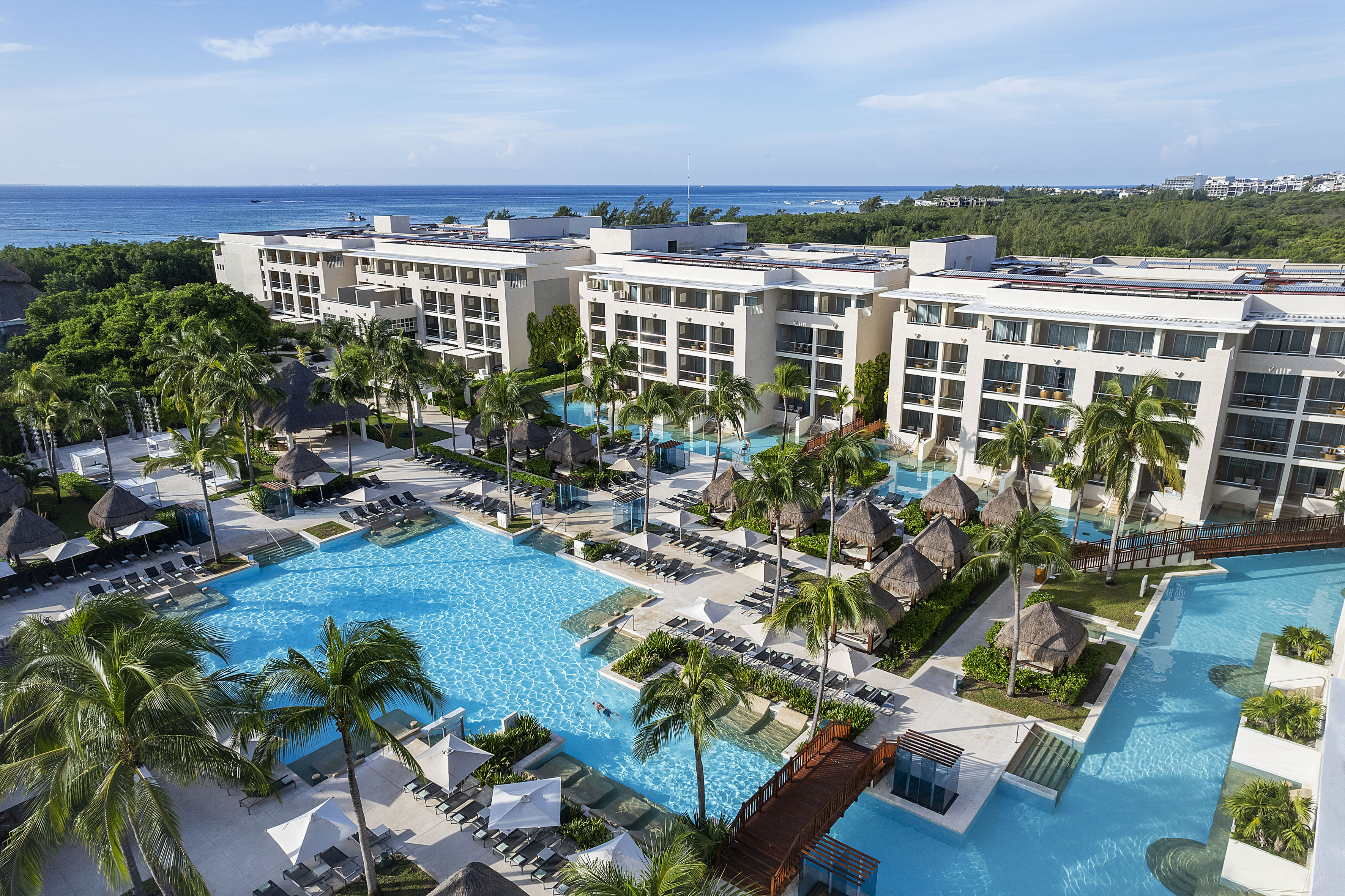 Aerial view: luxury tropical resort with multiple pools, palm trees, ocean.