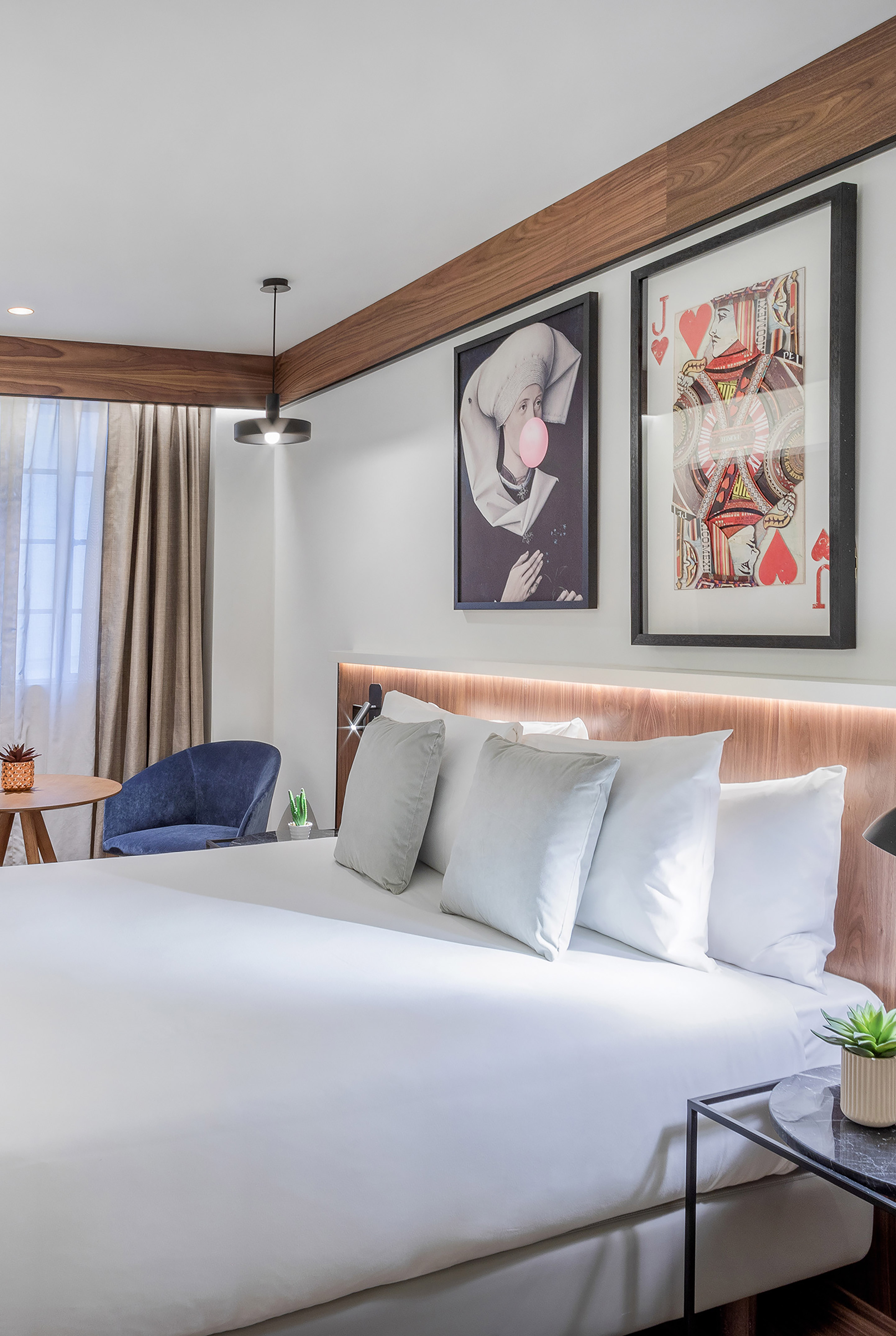 Modern hotel bedroom with white bed, wood headboard, pop art, and blue chair.