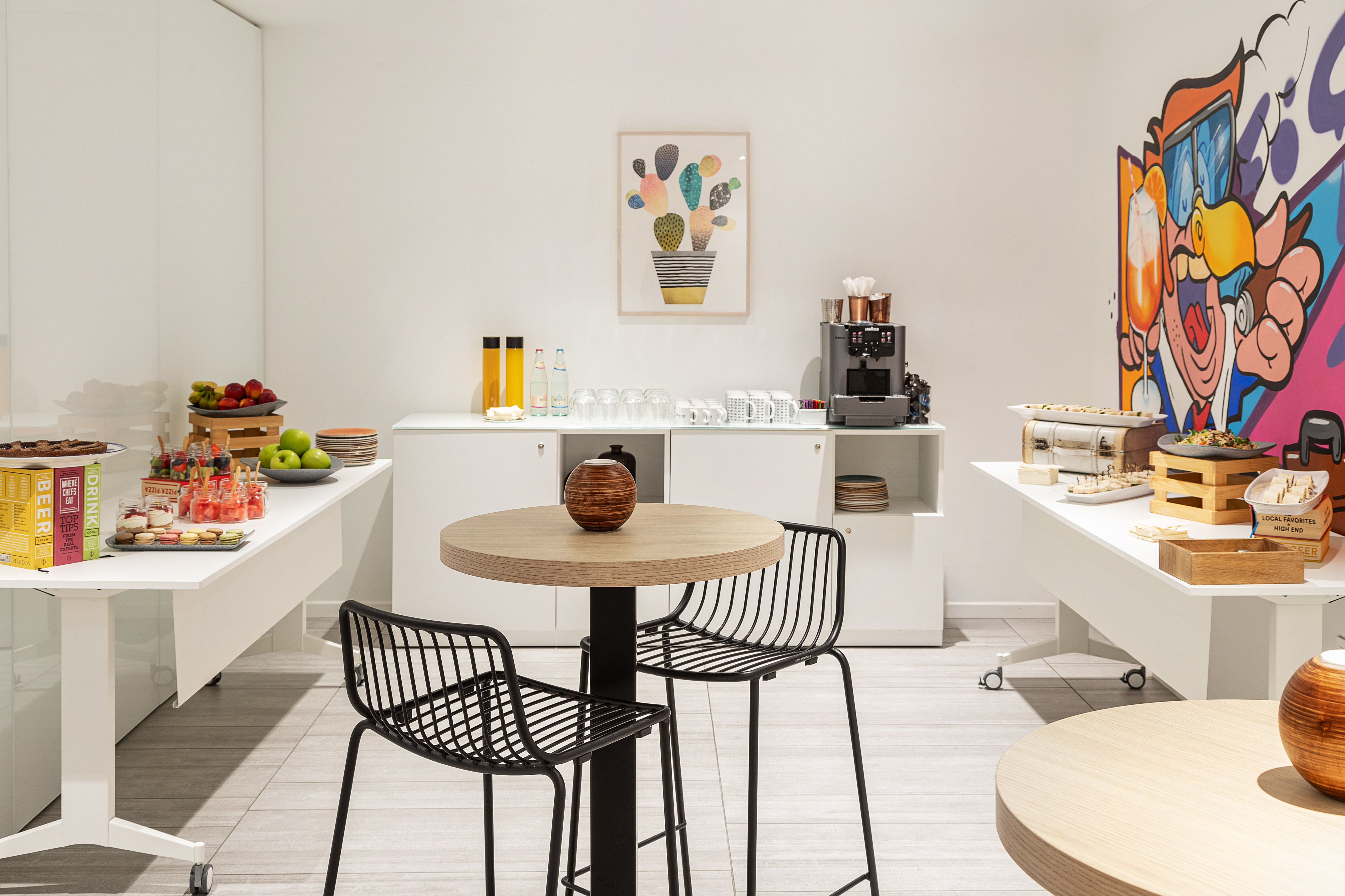 Modern office catering buffet with snacks, drinks, coffee, and casual seating.