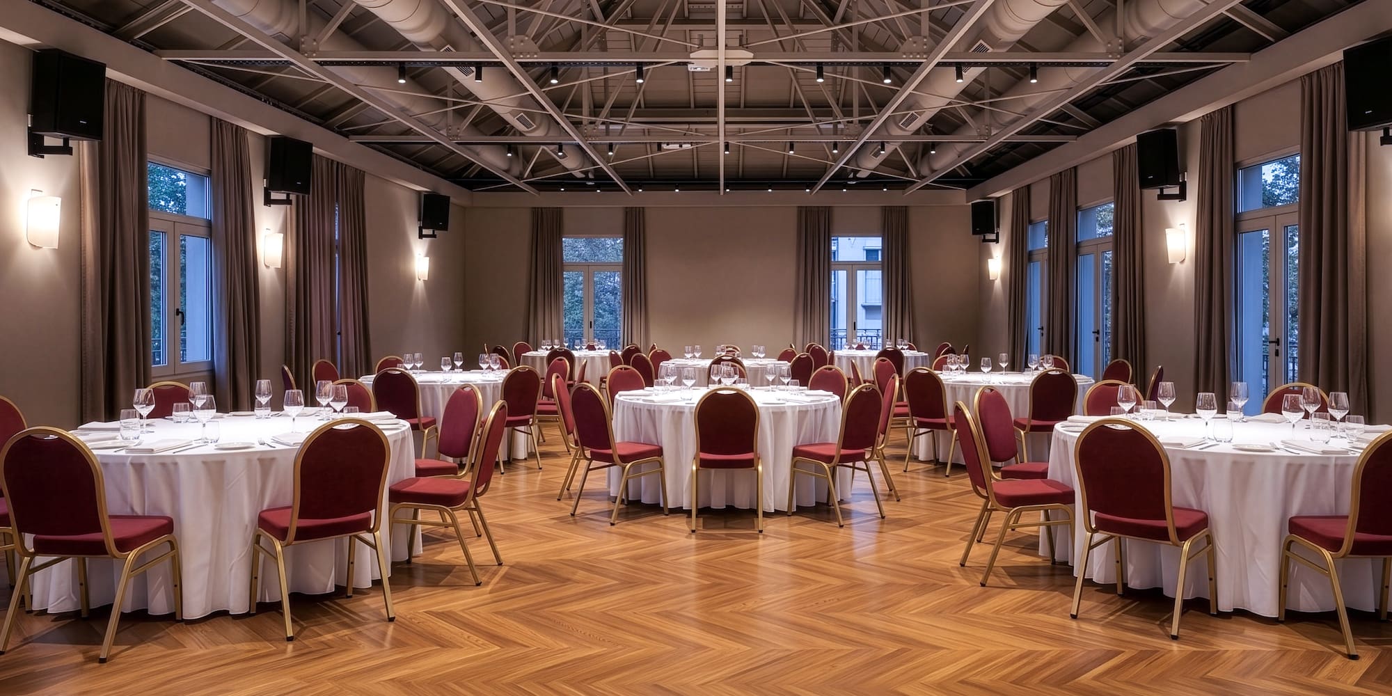 Elegant banquet hall with round tables, red chairs, and herringbone wood floor.
