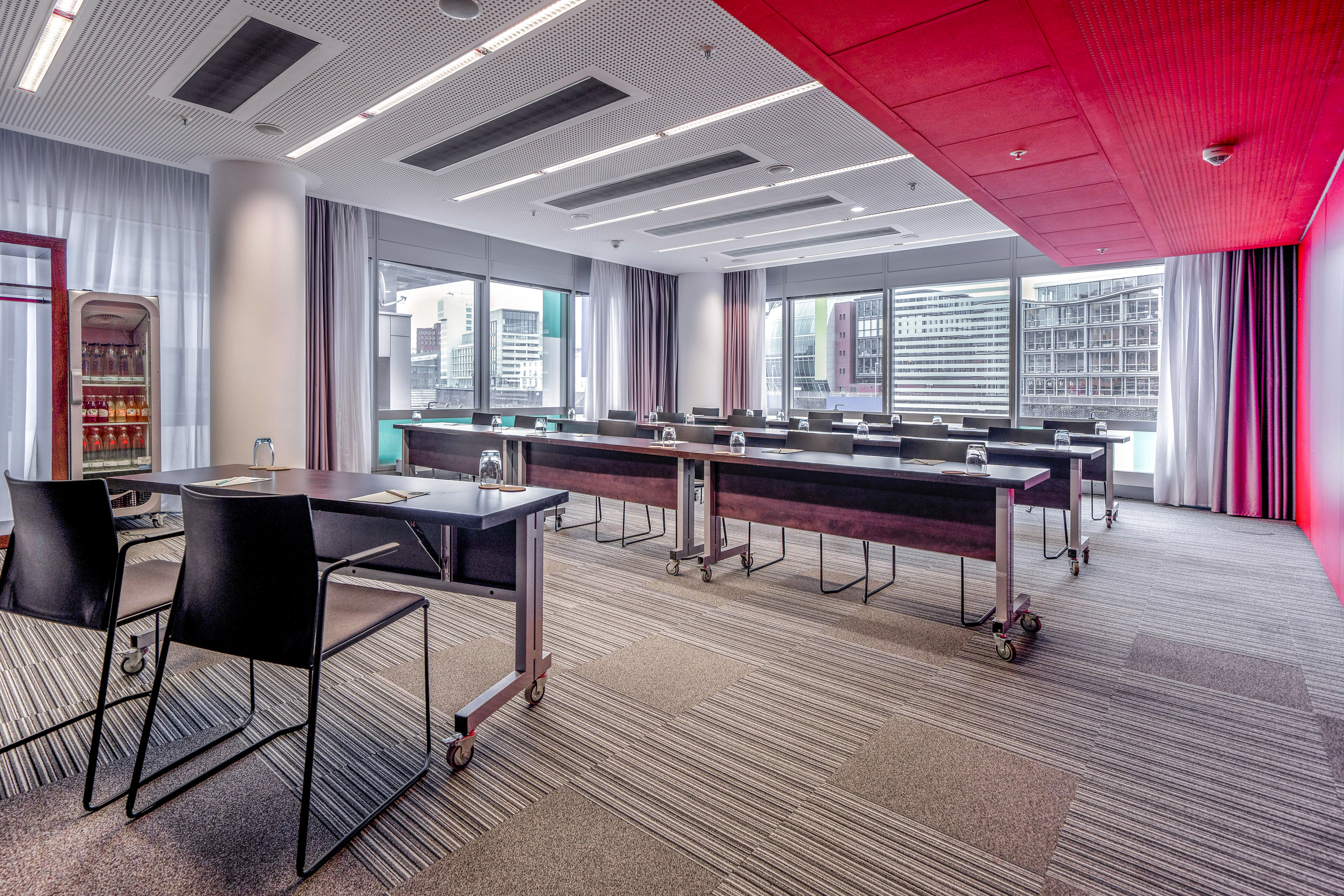 Modern conference room with red ceiling, large windows, and flexible tables.