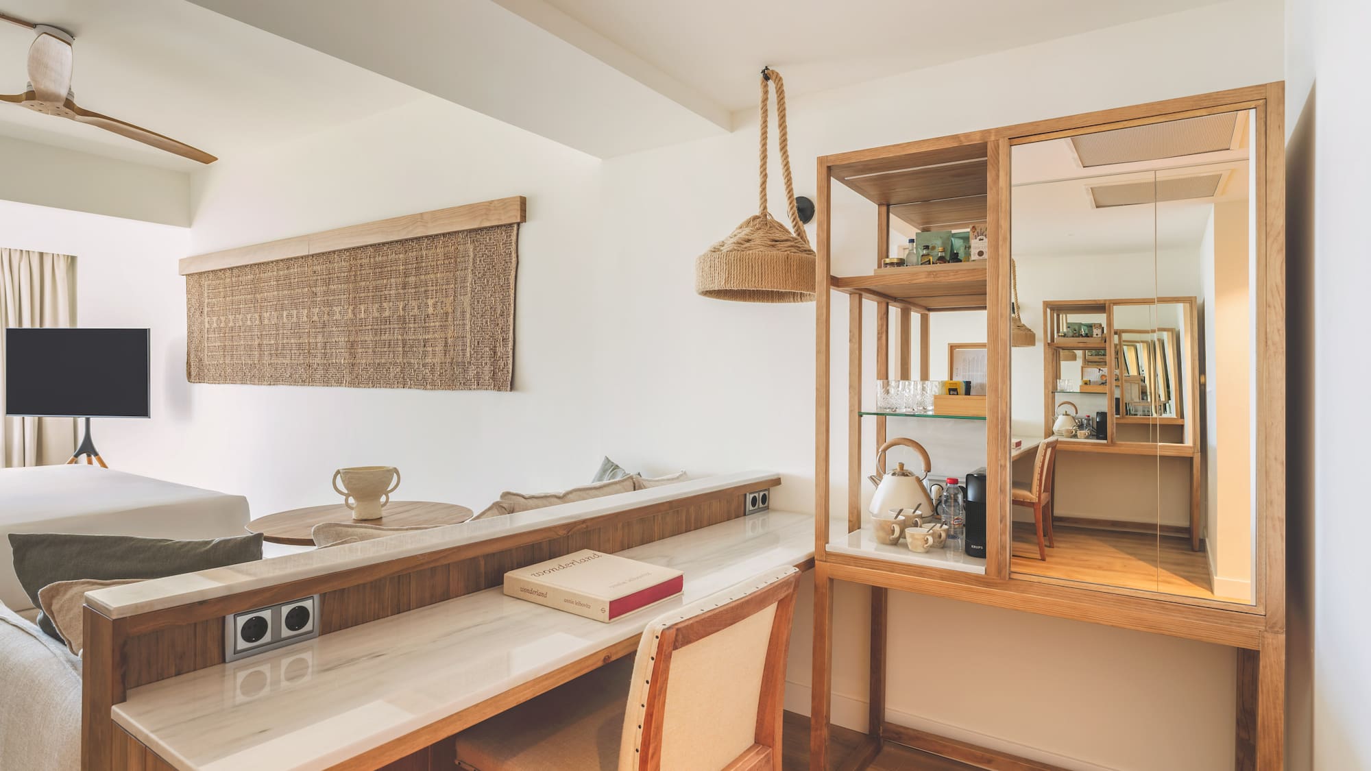 Modern hotel room with wooden desk, marble top, and natural decor.