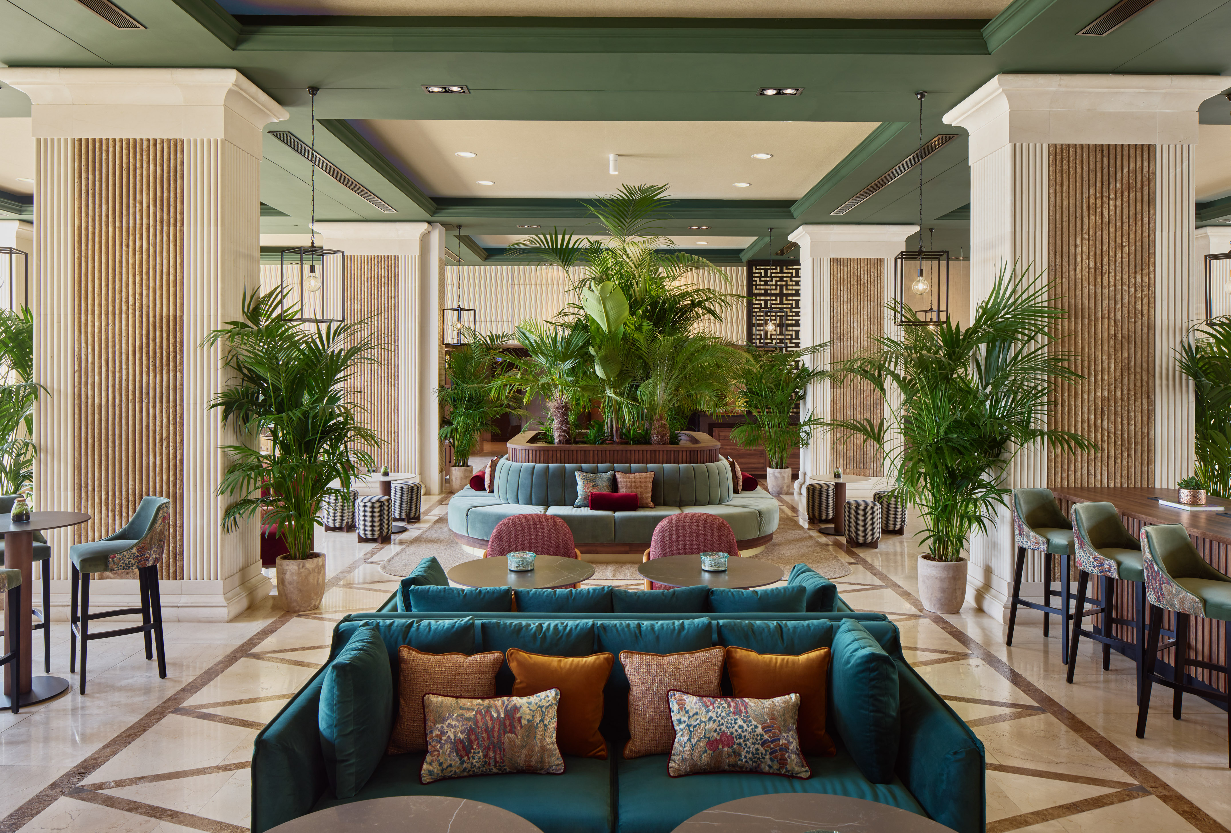 Luxurious hotel lounge with green velvet seating, lush plants, and elegant decor.