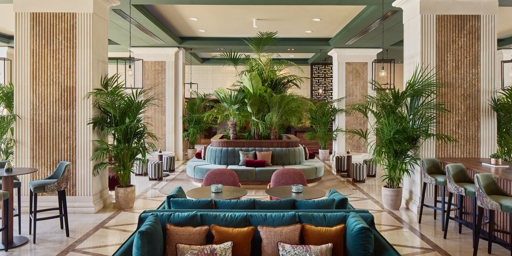 Luxurious hotel lounge with green velvet seating, lush plants, and elegant decor.