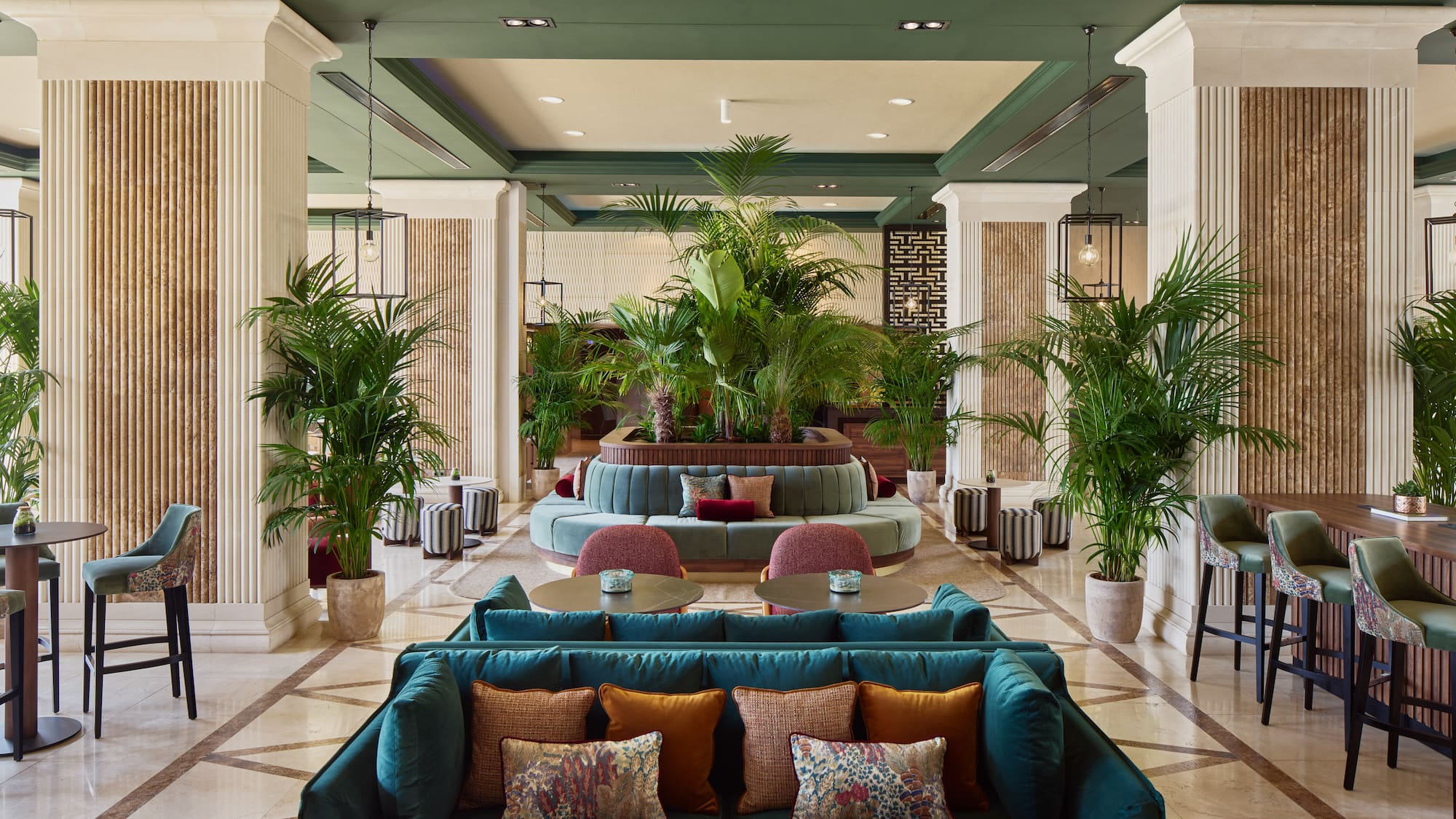 Luxurious hotel lounge with green velvet seating, lush plants, and elegant decor.