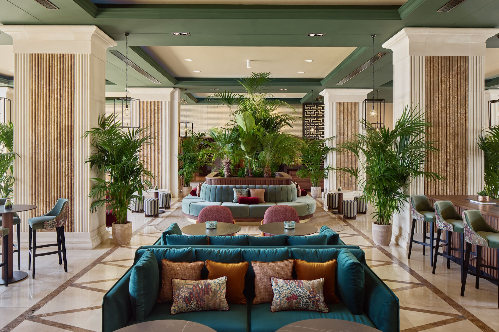 Luxurious hotel lounge with green velvet seating, lush plants, and elegant decor.