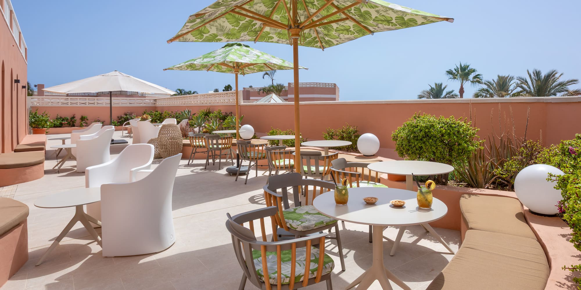 Sunny outdoor hotel patio with tropical umbrellas and modern seating.