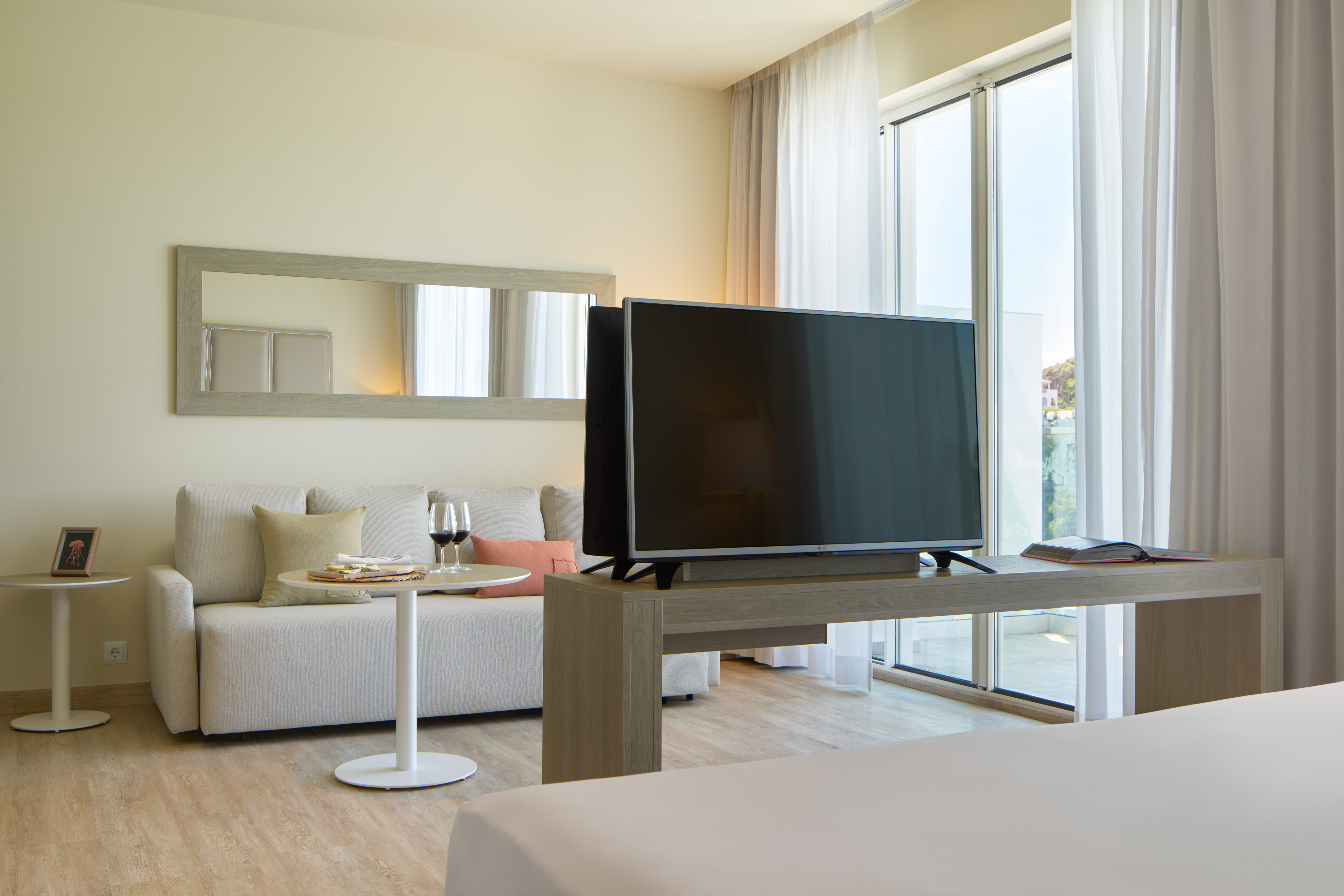 Bright modern hotel suite with sofa, flat-screen TV, and balcony access.