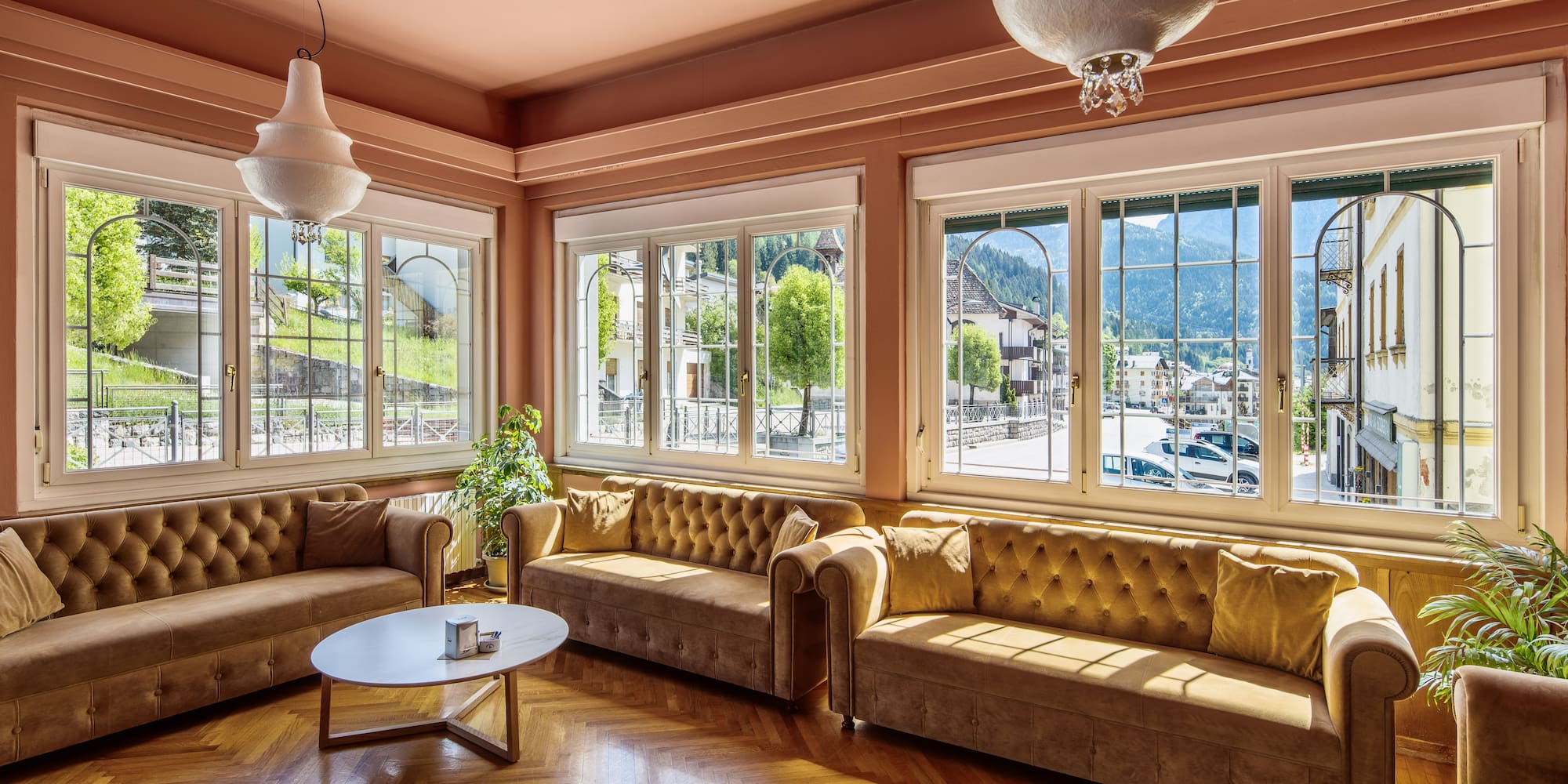 Sunlit living room with brown sofas, herringbone floor, mountain village views.